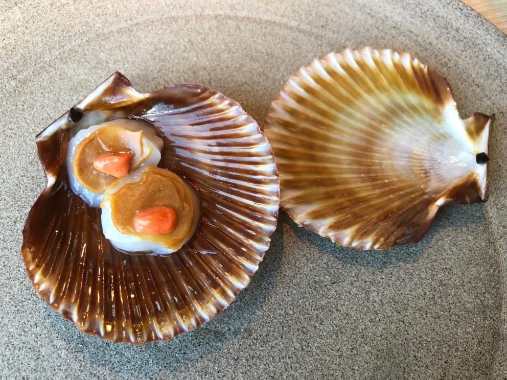 Photogallery






Noma 2.0 is in Christianshavn, the same neighbourhood as the first Noma. They’re 1.5 km apart, a 15 minutes’ walk. This picture shows the distance: to the right, there’s the warehouse of the old location (in Strandgade 93), to the left the smokestacks of Amager Bakke, the futuristic incinerator below which stands the new Noma (in Refshalevej 96)









Weather permitting, you can have a peaceful walk between the previous Noma to today’s Noma 









The new Noma is on an isthmus surrounded by canals. In the future they also want to reclaim some small parts for hydroponic farming









Bucolic scene with incinerator









Bikes left outside Noma. It’s the favourite means of transport among employees and interns









The long path taking you to the restaurant. The fence on the left shows how works are still in progress









On the two sides of the path there are the two new sections of the "Noma village", each with its specialty: grill, hot dishes, snacks, fermentations... In one month’s time, behind the fence we’ll have greenhouses, the test kitchen and the bread making area









To the left, before arriving at the restaurant, the future test kitchen. This will be run by Danish Mette Søberg with Riccardo Canella. "My first challenge?", reveals the latter, for a long time sous chef here, "is to work on the extraction of essential oils" 









The future Test Kitchen









The temporary gangway to the restaurant









Looking from the door to the restaurant, there’s a lake and the smokestacks puffing vapour from the Amager Bakke incinerator. It’s a futuristic project, both in terms of sustainability and architecture. It’s also known as Amager Slope or Copenhill, and its author is starchitect Bjarke Ingels, the same who designed the new Noma. Gradually opened in 2017, it transforms waste into electricity. The goal is to donate electricity to 62500 houses and hot water to 160000. It’s part of an ambitious project to transform Copenhagen into the first city in the world in terms of zero carbon dioxide emissions by 2025. By autumn this year, Amager Slope should open its ski slope, a climbing wall and a hiking track. You’ll be able to slalom on top of the incinerator









The windows from the dining room









Work is still in progress (photo taken on Thursday 22nd February 2018)









Traces of the old building, with barbwire. During WWII, they built bombs here









A view of the dining room at night (photo from Instagram/James Spreadbury)









The entrance to the restaurant









The usual ritual: a welcome from the entire staff, led by Rene Redzepi 









Behind the entrance, there are formaldehyde tanks with creatures from the abyss, shaped as in Damien Hirst’s works. The first image once you’re inside is to reproduce a Scandinavian village









The service kitchen is larger, more spacious and a completely open view from the dining room: "It’s the heart of our Scandinavian village", says Canella. There are 30 cooks working here now. 10 more, compared to the previous Noma









Large skylights above the cooks









There are currently more than 100 people working at Noma, of whom 63 are cooks - 26 employed, and 37 as interns









There’s fire in the kitchen, for the first time









On average, the dining room can host 40 people. "However", complains Redzepi, "there’s always someone who turns up with more people than the ones booked"









While the dining room is set, the outside space still need to be defined









The staff made the dining room decorations. There are no overly expensive designer objects









Dried fish









Seaweeds hanging from the ceiling









Dried octopus heads preserved in salt (with a balloon inside)














Bjarke Ingels and Redzepi’s plan included the wish to recreate a Danish farm









The luminous private dining room









The counter in the dining room. They drew the beams from the canals around the restaurant














The mise en place, bare and strictly without tablecloths









Water jug, candle, flower vase









A warm cloth, to begin with









Australian James Spreadbury, restaurant manager and partner at Noma









Welcome drink: Champagne extra brut Blanc d'Argile from Domaine Vouette et Sorbée









Sea Snail broth. The welcome dish at Noma is, as usual, a hot “soup”









Stefano Ferrano, from Torino, presents the following dish. There’s always a large Italian colony at Noma









Venus clams. Molluscs from Limfjord (Denmark) mixed with decorative clams, typical of Noma. Beside them, shells with blackcurrant oil and “Danish curry”, made with toasted coriander seeds, fennel and fennel seeds









The lid above the following dish. The mussels are not edible









Best of the mussel. Mussels open in a pan with water of fermented barley. «We recreate the mussel», says Canella, «using just the flaps, the best part». The paste is made with scraps from the mussel, cooked in smoked butter









The next dish is conceived and served by Riccardo Canella, the Paduan sous chef who conquered Redzepi, here with dining room intern Feline Hansen









Dried fruits and shrimps. In this case, the heads are not a decoration, but you must suck them –best not eat them because of the bones: they’re filled with a lovely prawn cream. The small crustaceans are still alive when they arrive on a ship straight from the Norwegian fjords









Inside, under the prawn broth skin, there’s fruits and vegetable preserved from the previous summer with raw prawns and gooseberry sauce with blackcurrant oil









How about beverages? There are three options, as usual: wine pairing (6 glasses plus a beer plus sake, 150 euros), juice pairing (juices and extracts, 110 euros) or a choice from the list. They recommend Champagne Chut... Libre from Val'Frison pour Dominique Derain, 50% Pinot Noir, 50% Chardonnay created by a couple who met at the old Noma. Well bodied, it will be a good match throughout the meal









As usual, the wine list starts with Champagne: the cheapest is 1400 crowns (190 euros)









White wines begin with labels from cold climates: first Austria, increasingly popular for its natural wines, then Germany, then all the others









How about Italy? Few names, among the white wines, from North and South









A dozen red/orange wines









Sea star, that is to say Cured trout roe and eggs, the emblem dish of this new era. They recommend moving the teaspoon from the heart to the edges of the tentacles. Aesthetics win over taste









Jellyfish. The jellyfish gel in the middle is in fact a clarified broth of calamari and recalls the texture of jellyfish. "We tried to cook jellyfish in 300 different ways but none was convincing so far". All around, pickled seaweed. The gel is almost tasteless, it serves to clean the palate after the pickles









Rene Redzepi himself presents the content of the first Seafood platter.









French style service with a small plate below for the empty shells









It’s made of two (per two) pieces: queen clam and mahogany clam






