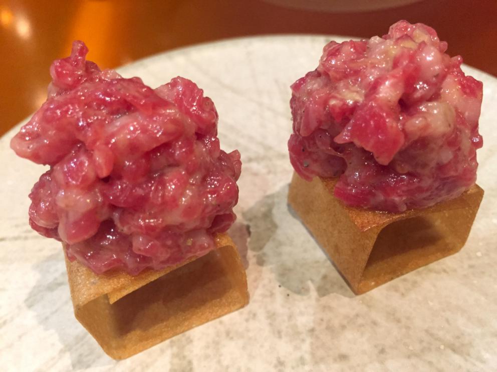 Galleria fotografica






Consommè de garbanzos. Prima che cominci il menu degustazione, viene portata al tavolo una bottiglia di vetro contenente del brodo freddo di ceci (in alto a destra). Ventitrè piatti dopo, alla fine del percorso "salato", verrà versato, in un bicchierino da grappa, del brodo caldo di jamon iberico da una teiera. Sopra ancora, la schiuma del brodo di ceci. Un caldo-freddo speciale (foto @ticketsbar instagram)









Tosta de pollo y anchoa. Primo piatto: toast di pelle di pollo con lisca di acciuga. A lato, una crema di acciughe composta da burro e pasta di acciughe









Olive Gordal. Uno dei simboli della saga Adrià: le olive sono immerse in un liquido d'olio extravergine d'oliva, cannella, buccia di limone e anice stellato. Si tirano su con un cucchiaino forato, si poggiano su una conchiglia di legno a lato e da qui in bocca. Gordal è una varietà dall'Andalusia









Prima preparazione rifinita al tavolo: Polo de almendras









Polo de almendras è uno stecco di gelato al latte di mandorle, spennellato sul posto con olio d'oliva e cosparso con granelle di mandorle, fiori di sambuco e sale. E' servito su un piatto con cubetti di ghiaccio. Dolce(salato) e gelato all'inizio del pasto e non alla fine, uno schema molto Adrià









Coliflor y caviar. Ganache di cavolfiore e caviale russo Schrenkii









Gamba a la sal fría. Gamberi marinati nel tè Lapsang Souchong con zest di bergamotto. Sono serviti su un vassoio con "neve di sale" per ricordare il ghiaccio tipico di un mercato del pesce









Atún con cerezas. Tonno e ciliegia: ventresca di tonno confit in grasso di prosciutto, accompagnata da una ciliegia affumicata (senza nocciolo)









Ceviche de melón cantaloup. Ceviche di melone cantalupo con succo di lime, coriandolo e leche de tigre di kumquat. Servito con kumquat, olio di coriandolo e neve di kumquat. Citrico alla terza









Pizza crujiente. La "pizza" di Tickets: millefoglie di regañà (torta di pane croccante di origini andaluse), stracciatella, bottarga e fichi









Porex de Calix. Marshmallow di dashi ripieno di crema acida e sormontato da caviale di Kalix, uova rosse svedesi di coregone, dalle note dolci ed eleganti









Nigiri de berenjena. Nigiri di melanzana






