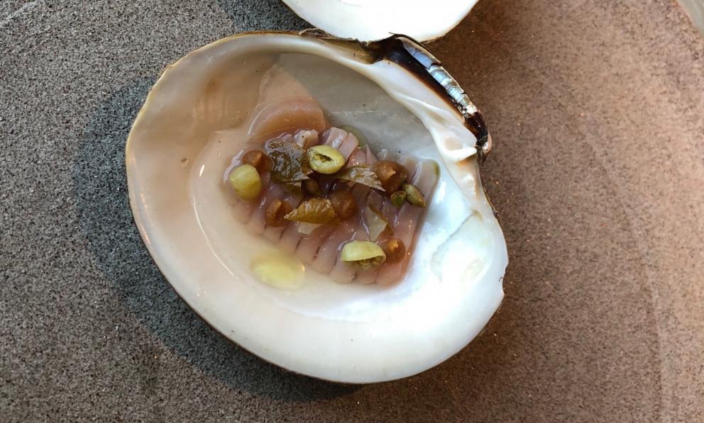 Photogallery






Noma 2.0 is in Christianshavn, the same neighbourhood as the first Noma. They’re 1.5 km apart, a 15 minutes’ walk. This picture shows the distance: to the right, there’s the warehouse of the old location (in Strandgade 93), to the left the smokestacks of Amager Bakke, the futuristic incinerator below which stands the new Noma (in Refshalevej 96)









Weather permitting, you can have a peaceful walk between the previous Noma to today’s Noma 









The new Noma is on an isthmus surrounded by canals. In the future they also want to reclaim some small parts for hydroponic farming









Bucolic scene with incinerator









Bikes left outside Noma. It’s the favourite means of transport among employees and interns









The long path taking you to the restaurant. The fence on the left shows how works are still in progress









On the two sides of the path there are the two new sections of the "Noma village", each with its specialty: grill, hot dishes, snacks, fermentations... In one month’s time, behind the fence we’ll have greenhouses, the test kitchen and the bread making area









To the left, before arriving at the restaurant, the future test kitchen. This will be run by Danish Mette Søberg with Riccardo Canella. "My first challenge?", reveals the latter, for a long time sous chef here, "is to work on the extraction of essential oils" 









The future Test Kitchen









The temporary gangway to the restaurant









Looking from the door to the restaurant, there’s a lake and the smokestacks puffing vapour from the Amager Bakke incinerator. It’s a futuristic project, both in terms of sustainability and architecture. It’s also known as Amager Slope or Copenhill, and its author is starchitect Bjarke Ingels, the same who designed the new Noma. Gradually opened in 2017, it transforms waste into electricity. The goal is to donate electricity to 62500 houses and hot water to 160000. It’s part of an ambitious project to transform Copenhagen into the first city in the world in terms of zero carbon dioxide emissions by 2025. By autumn this year, Amager Slope should open its ski slope, a climbing wall and a hiking track. You’ll be able to slalom on top of the incinerator









The windows from the dining room









Work is still in progress (photo taken on Thursday 22nd February 2018)









Traces of the old building, with barbwire. During WWII, they built bombs here









A view of the dining room at night (photo from Instagram/James Spreadbury)









The entrance to the restaurant









The usual ritual: a welcome from the entire staff, led by Rene Redzepi 









Behind the entrance, there are formaldehyde tanks with creatures from the abyss, shaped as in Damien Hirst’s works. The first image once you’re inside is to reproduce a Scandinavian village









The service kitchen is larger, more spacious and a completely open view from the dining room: "It’s the heart of our Scandinavian village", says Canella. There are 30 cooks working here now. 10 more, compared to the previous Noma









Large skylights above the cooks









There are currently more than 100 people working at Noma, of whom 63 are cooks - 26 employed, and 37 as interns









There’s fire in the kitchen, for the first time









On average, the dining room can host 40 people. "However", complains Redzepi, "there’s always someone who turns up with more people than the ones booked"









While the dining room is set, the outside space still need to be defined









The staff made the dining room decorations. There are no overly expensive designer objects









Dried fish









Seaweeds hanging from the ceiling









Dried octopus heads preserved in salt (with a balloon inside)














Bjarke Ingels and Redzepi’s plan included the wish to recreate a Danish farm









The luminous private dining room









The counter in the dining room. They drew the beams from the canals around the restaurant














The mise en place, bare and strictly without tablecloths









Water jug, candle, flower vase









A warm cloth, to begin with









Australian James Spreadbury, restaurant manager and partner at Noma









Welcome drink: Champagne extra brut Blanc d'Argile from Domaine Vouette et Sorbée









Sea Snail broth. The welcome dish at Noma is, as usual, a hot “soup”









Stefano Ferrano, from Torino, presents the following dish. There’s always a large Italian colony at Noma









Venus clams. Molluscs from Limfjord (Denmark) mixed with decorative clams, typical of Noma. Beside them, shells with blackcurrant oil and “Danish curry”, made with toasted coriander seeds, fennel and fennel seeds









The lid above the following dish. The mussels are not edible









Best of the mussel. Mussels open in a pan with water of fermented barley. «We recreate the mussel», says Canella, «using just the flaps, the best part». The paste is made with scraps from the mussel, cooked in smoked butter









The next dish is conceived and served by Riccardo Canella, the Paduan sous chef who conquered Redzepi, here with dining room intern Feline Hansen









Dried fruits and shrimps. In this case, the heads are not a decoration, but you must suck them –best not eat them because of the bones: they’re filled with a lovely prawn cream. The small crustaceans are still alive when they arrive on a ship straight from the Norwegian fjords









Inside, under the prawn broth skin, there’s fruits and vegetable preserved from the previous summer with raw prawns and gooseberry sauce with blackcurrant oil









How about beverages? There are three options, as usual: wine pairing (6 glasses plus a beer plus sake, 150 euros), juice pairing (juices and extracts, 110 euros) or a choice from the list. They recommend Champagne Chut... Libre from Val'Frison pour Dominique Derain, 50% Pinot Noir, 50% Chardonnay created by a couple who met at the old Noma. Well bodied, it will be a good match throughout the meal









As usual, the wine list starts with Champagne: the cheapest is 1400 crowns (190 euros)









White wines begin with labels from cold climates: first Austria, increasingly popular for its natural wines, then Germany, then all the others









How about Italy? Few names, among the white wines, from North and South









A dozen red/orange wines









Sea star, that is to say Cured trout roe and eggs, the emblem dish of this new era. They recommend moving the teaspoon from the heart to the edges of the tentacles. Aesthetics win over taste









Jellyfish. The jellyfish gel in the middle is in fact a clarified broth of calamari and recalls the texture of jellyfish. "We tried to cook jellyfish in 300 different ways but none was convincing so far". All around, pickled seaweed. The gel is almost tasteless, it serves to clean the palate after the pickles









Rene Redzepi himself presents the content of the first Seafood platter.









French style service with a small plate below for the empty shells









It’s made of two (per two) pieces: queen clam and mahogany clam









The Queen Clam is a very small variety of Norwegian scallop, seasoned with a vegetal reduction made with cucumber and peas miso. The red tip is the coral. "You should eat it using the top shell ", recommends Redzepi









The Mahogany clam is a centennial clam from the North Sea, very popular in Denmark and Iceland. «You can tell the age by the number of rings, like with trees», says Redzepi, «In 2007 they found one that was 450 years old. We’ve had it in the menu for a decade or so». The razor clam shell serves as teaspoon






