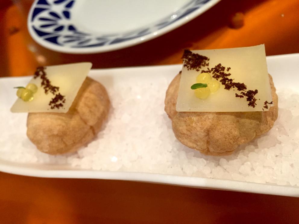 Galleria fotografica






Consommè de garbanzos. Prima che cominci il menu degustazione, viene portata al tavolo una bottiglia di vetro contenente del brodo freddo di ceci (in alto a destra). Ventitrè piatti dopo, alla fine del percorso "salato", verrà versato, in un bicchierino da grappa, del brodo caldo di jamon iberico da una teiera. Sopra ancora, la schiuma del brodo di ceci. Un caldo-freddo speciale (foto @ticketsbar instagram)









Tosta de pollo y anchoa. Primo piatto: toast di pelle di pollo con lisca di acciuga. A lato, una crema di acciughe composta da burro e pasta di acciughe









Olive Gordal. Uno dei simboli della saga Adrià: le olive sono immerse in un liquido d'olio extravergine d'oliva, cannella, buccia di limone e anice stellato. Si tirano su con un cucchiaino forato, si poggiano su una conchiglia di legno a lato e da qui in bocca. Gordal è una varietà dall'Andalusia









Prima preparazione rifinita al tavolo: Polo de almendras









Polo de almendras è uno stecco di gelato al latte di mandorle, spennellato sul posto con olio d'oliva e cosparso con granelle di mandorle, fiori di sambuco e sale. E' servito su un piatto con cubetti di ghiaccio. Dolce(salato) e gelato all'inizio del pasto e non alla fine, uno schema molto Adrià









Coliflor y caviar. Ganache di cavolfiore e caviale russo Schrenkii









Gamba a la sal fría. Gamberi marinati nel tè Lapsang Souchong con zest di bergamotto. Sono serviti su un vassoio con "neve di sale" per ricordare il ghiaccio tipico di un mercato del pesce









Atún con cerezas. Tonno e ciliegia: ventresca di tonno confit in grasso di prosciutto, accompagnata da una ciliegia affumicata (senza nocciolo)









Ceviche de melón cantaloup. Ceviche di melone cantalupo con succo di lime, coriandolo e leche de tigre di kumquat. Servito con kumquat, olio di coriandolo e neve di kumquat. Citrico alla terza









Pizza crujiente. La "pizza" di Tickets: millefoglie di regañà (torta di pane croccante di origini andaluse), stracciatella, bottarga e fichi









Porex de Calix. Marshmallow di dashi ripieno di crema acida e sormontato da caviale di Kalix, uova rosse svedesi di coregone, dalle note dolci ed eleganti









Nigiri de berenjena. Nigiri di melanzana









Cubo de wagyu. Cubo di chips di patata croccante con sopra una tartare di wagyu trattata con olio, sale, senape di Digione, uova e pepe. Una magnifica tapa da circa 2 cm per lato, che ricorda le battute al coltello della tradizione piemontese









Milhojas de atún. Millefoglie di tonno: millefoglie di patata e alga nori. In cima, tartare di tonno leggermente piccante con crema di avocado






