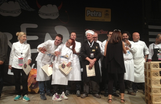 Galleria fotograficaFabio Pisani di Aimo e Nadia e il suo partner della rassegna, Davide Longoni del panificio LongoniPer Pisani e Longoni, un'apprezzatissima Rosetta di Petra con cicerchie, ciocriette selvatiche e ricotta marzoticaMarco Valletta dell'Accademia del pane e Maria Grazia Attolini della Dolcetteria di Rimini. Per loro Tondo morbido di glutin&ograve; all'origano con polpa di trota del Sile e zucchine marinate all'agretto&nbsp;(foto Sarah Scaparone)Aurora Mazzucchelli del ristorante Marconi di Sasso Marconi (Bologna) era in coppia con Massimo Vitali del panificio Vitali di Cesenatico (Forl&igrave;-Cesena)Per loro anche un insolito tocco di cioccolato tra due fette di Ciabattina di Petra con fiocchi di germe di grano, ripiene anche di formaggio ragusano, origano sicliano e olive fresche. Rievocazione di memorie d'infanzia per la MazzucchelliSimone Padoan de I Tigli di San Bonifacio (Verona) era in tandem con Pietro Freddi dell'omonima forneria di Casto (Brescia)Per loro, un Tondo morbido di Petra con farina di piselli germinati con tonno, ruchetta, cipolla in carpione, alga nori e yogurt alla senape. Un hot dog di tonno, insomma, quello di Padoan/Freddi, giocato sul concetto di "maiale del mare"Marco Stabile dell'Ora d'Aria di Firenze e Alessio Cecchi dell'Antico Forno Bacci di Campi Bisenzio (Firenze)Stabile/Cecchi: Ciabattina di Petra, mortadella di Prato, cavolo cappuccio, pecorino marzolino, scorza di lime e ketchup di peperoni (foto Sarah Scaparone)Lionello Cera dell'Antica Osteria Cera di Campagna Lupia (Venezia), in coppia con Nicola Trentin de Le Delizie del Grano di Cittadella (Padova)Alessandro Spoto di Voglia di Pane (Torino) ed Eugenio Roncoroni de Al Mercato di Milano. Per loro una Piadina di farina di grano saraceno germinato (brick 1240) con fegatini di pollo, lattuga, senape e salsa tailandese piccante agrodolcePiazza Maggiore, salotto estenseUn panino fusion nord-sud: Pagnottina cafona di Petra con capocollo e mozzarella di bufala campana Dop. L'hanno assemblato assieme Raffaele Vitale di Casa del Nonno 13 (Mercato San Severino, Salerno) e Paolo Piantoni del Panificio El Forner di BresciaFabio Pisani di Aimo e Nadia e Andrea Paternoster, la mente di Mieli Thun, ora alle prese anche con un aceto di miele al rosmarinoTondo di Petra con farina di piselli germinati, ripieno di panzia di maiale, pomodoro datterino, cipolla di Tropea e senape di Giorgio e Gianpietro Damini di Damini e Affini, in coppia con Matteo Piffer del Panificio Moderno di Isera (Trento) (foto Sarah Scaparone)C'era anche un panino vegano (non col seitan). L'hanno firmato Lello Ravagnan della Pizzeria Grigoris di Asseggiano (Venezia) e Luca Scarcella de Il Forno dell'Angolo di Torino: Tondo morbido di Petra con farina di piselli germinati (Brick 1150), ceci, lenticchie e peperone in maionese vegetale (foto Sarah Scaparone)La Rosetta di Petra con farina di grano saraceno germinato con costine di maiale, melanzane e patate al vapore dei fratelli Nicola e Luigi Portinari della Peca di Lonigo (Vicenza) con Giuseppe Vicentini del Panificio Vicentini di Maragnole)Il Tondo morbido con ricotta gelata, scaglie di pistacchio e profumo d'agrumi. Un gettonatissimo panino/dessert firmato da Pina Toscani del Progetto Sunread di Mestre (Venezia) e Alessandro Lunardi di Nuvola Rossa a Brugine (Padova)Bread Religion &egrave; stata ravvivata dal sound dei ragazzi del Mangiadischi (cui dobbiamo il copyright di questa foto). Da sinistra, Andy, leader della band Fluon, Carlo Spinelli e Niccolo Vecchia