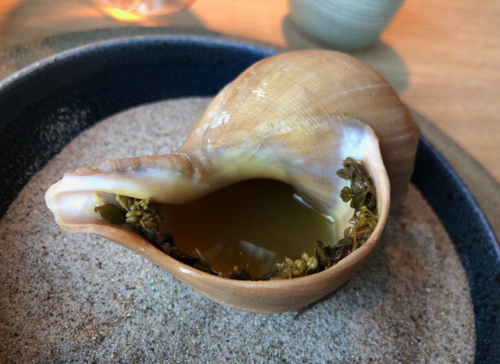 Photogallery






Noma 2.0 is in Christianshavn, the same neighbourhood as the first Noma. They’re 1.5 km apart, a 15 minutes’ walk. This picture shows the distance: to the right, there’s the warehouse of the old location (in Strandgade 93), to the left the smokestacks of Amager Bakke, the futuristic incinerator below which stands the new Noma (in Refshalevej 96)









Weather permitting, you can have a peaceful walk between the previous Noma to today’s Noma 









The new Noma is on an isthmus surrounded by canals. In the future they also want to reclaim some small parts for hydroponic farming









Bucolic scene with incinerator









Bikes left outside Noma. It’s the favourite means of transport among employees and interns









The long path taking you to the restaurant. The fence on the left shows how works are still in progress









On the two sides of the path there are the two new sections of the "Noma village", each with its specialty: grill, hot dishes, snacks, fermentations... In one month’s time, behind the fence we’ll have greenhouses, the test kitchen and the bread making area









To the left, before arriving at the restaurant, the future test kitchen. This will be run by Danish Mette Søberg with Riccardo Canella. "My first challenge?", reveals the latter, for a long time sous chef here, "is to work on the extraction of essential oils" 









The future Test Kitchen









The temporary gangway to the restaurant









Looking from the door to the restaurant, there’s a lake and the smokestacks puffing vapour from the Amager Bakke incinerator. It’s a futuristic project, both in terms of sustainability and architecture. It’s also known as Amager Slope or Copenhill, and its author is starchitect Bjarke Ingels, the same who designed the new Noma. Gradually opened in 2017, it transforms waste into electricity. The goal is to donate electricity to 62500 houses and hot water to 160000. It’s part of an ambitious project to transform Copenhagen into the first city in the world in terms of zero carbon dioxide emissions by 2025. By autumn this year, Amager Slope should open its ski slope, a climbing wall and a hiking track. You’ll be able to slalom on top of the incinerator









The windows from the dining room









Work is still in progress (photo taken on Thursday 22nd February 2018)









Traces of the old building, with barbwire. During WWII, they built bombs here









A view of the dining room at night (photo from Instagram/James Spreadbury)









The entrance to the restaurant









The usual ritual: a welcome from the entire staff, led by Rene Redzepi 









Behind the entrance, there are formaldehyde tanks with creatures from the abyss, shaped as in Damien Hirst’s works. The first image once you’re inside is to reproduce a Scandinavian village









The service kitchen is larger, more spacious and a completely open view from the dining room: "It’s the heart of our Scandinavian village", says Canella. There are 30 cooks working here now. 10 more, compared to the previous Noma









Large skylights above the cooks









There are currently more than 100 people working at Noma, of whom 63 are cooks - 26 employed, and 37 as interns









There’s fire in the kitchen, for the first time









On average, the dining room can host 40 people. "However", complains Redzepi, "there’s always someone who turns up with more people than the ones booked"









While the dining room is set, the outside space still need to be defined









The staff made the dining room decorations. There are no overly expensive designer objects









Dried fish









Seaweeds hanging from the ceiling









Dried octopus heads preserved in salt (with a balloon inside)














Bjarke Ingels and Redzepi’s plan included the wish to recreate a Danish farm









The luminous private dining room









The counter in the dining room. They drew the beams from the canals around the restaurant














The mise en place, bare and strictly without tablecloths









Water jug, candle, flower vase









A warm cloth, to begin with









Australian James Spreadbury, restaurant manager and partner at Noma









Welcome drink: Champagne extra brut Blanc d'Argile from Domaine Vouette et Sorbée






