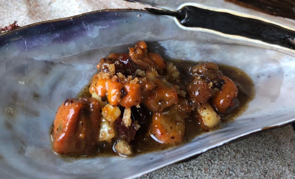 Photogallery






Noma 2.0 is in Christianshavn, the same neighbourhood as the first Noma. They’re 1.5 km apart, a 15 minutes’ walk. This picture shows the distance: to the right, there’s the warehouse of the old location (in Strandgade 93), to the left the smokestacks of Amager Bakke, the futuristic incinerator below which stands the new Noma (in Refshalevej 96)









Weather permitting, you can have a peaceful walk between the previous Noma to today’s Noma 









The new Noma is on an isthmus surrounded by canals. In the future they also want to reclaim some small parts for hydroponic farming









Bucolic scene with incinerator









Bikes left outside Noma. It’s the favourite means of transport among employees and interns









The long path taking you to the restaurant. The fence on the left shows how works are still in progress









On the two sides of the path there are the two new sections of the "Noma village", each with its specialty: grill, hot dishes, snacks, fermentations... In one month’s time, behind the fence we’ll have greenhouses, the test kitchen and the bread making area









To the left, before arriving at the restaurant, the future test kitchen. This will be run by Danish Mette Søberg with Riccardo Canella. "My first challenge?", reveals the latter, for a long time sous chef here, "is to work on the extraction of essential oils" 









The future Test Kitchen









The temporary gangway to the restaurant









Looking from the door to the restaurant, there’s a lake and the smokestacks puffing vapour from the Amager Bakke incinerator. It’s a futuristic project, both in terms of sustainability and architecture. It’s also known as Amager Slope or Copenhill, and its author is starchitect Bjarke Ingels, the same who designed the new Noma. Gradually opened in 2017, it transforms waste into electricity. The goal is to donate electricity to 62500 houses and hot water to 160000. It’s part of an ambitious project to transform Copenhagen into the first city in the world in terms of zero carbon dioxide emissions by 2025. By autumn this year, Amager Slope should open its ski slope, a climbing wall and a hiking track. You’ll be able to slalom on top of the incinerator









The windows from the dining room









Work is still in progress (photo taken on Thursday 22nd February 2018)









Traces of the old building, with barbwire. During WWII, they built bombs here









A view of the dining room at night (photo from Instagram/James Spreadbury)









The entrance to the restaurant









The usual ritual: a welcome from the entire staff, led by Rene Redzepi 









Behind the entrance, there are formaldehyde tanks with creatures from the abyss, shaped as in Damien Hirst’s works. The first image once you’re inside is to reproduce a Scandinavian village









The service kitchen is larger, more spacious and a completely open view from the dining room: "It’s the heart of our Scandinavian village", says Canella. There are 30 cooks working here now. 10 more, compared to the previous Noma









Large skylights above the cooks









There are currently more than 100 people working at Noma, of whom 63 are cooks - 26 employed, and 37 as interns









There’s fire in the kitchen, for the first time









On average, the dining room can host 40 people. "However", complains Redzepi, "there’s always someone who turns up with more people than the ones booked"









While the dining room is set, the outside space still need to be defined









The staff made the dining room decorations. There are no overly expensive designer objects









Dried fish









Seaweeds hanging from the ceiling









Dried octopus heads preserved in salt (with a balloon inside)














Bjarke Ingels and Redzepi’s plan included the wish to recreate a Danish farm









The luminous private dining room









The counter in the dining room. They drew the beams from the canals around the restaurant














The mise en place, bare and strictly without tablecloths









Water jug, candle, flower vase









A warm cloth, to begin with









Australian James Spreadbury, restaurant manager and partner at Noma









Welcome drink: Champagne extra brut Blanc d'Argile from Domaine Vouette et Sorbée









Sea Snail broth. The welcome dish at Noma is, as usual, a hot “soup”









Stefano Ferrano, from Torino, presents the following dish. There’s always a large Italian colony at Noma









Venus clams. Molluscs from Limfjord (Denmark) mixed with decorative clams, typical of Noma. Beside them, shells with blackcurrant oil and “Danish curry”, made with toasted coriander seeds, fennel and fennel seeds









The lid above the following dish. The mussels are not edible









Best of the mussel. Mussels open in a pan with water of fermented barley. «We recreate the mussel», says Canella, «using just the flaps, the best part». The paste is made with scraps from the mussel, cooked in smoked butter









The next dish is conceived and served by Riccardo Canella, the Paduan sous chef who conquered Redzepi, here with dining room intern Feline Hansen









Dried fruits and shrimps. In this case, the heads are not a decoration, but you must suck them –best not eat them because of the bones: they’re filled with a lovely prawn cream. The small crustaceans are still alive when they arrive on a ship straight from the Norwegian fjords









Inside, under the prawn broth skin, there’s fruits and vegetable preserved from the previous summer with raw prawns and gooseberry sauce with blackcurrant oil









How about beverages? There are three options, as usual: wine pairing (6 glasses plus a beer plus sake, 150 euros), juice pairing (juices and extracts, 110 euros) or a choice from the list. They recommend Champagne Chut... Libre from Val'Frison pour Dominique Derain, 50% Pinot Noir, 50% Chardonnay created by a couple who met at the old Noma. Well bodied, it will be a good match throughout the meal









As usual, the wine list starts with Champagne: the cheapest is 1400 crowns (190 euros)









White wines begin with labels from cold climates: first Austria, increasingly popular for its natural wines, then Germany, then all the others









How about Italy? Few names, among the white wines, from North and South









A dozen red/orange wines









Sea star, that is to say Cured trout roe and eggs, the emblem dish of this new era. They recommend moving the teaspoon from the heart to the edges of the tentacles. Aesthetics win over taste









Jellyfish. The jellyfish gel in the middle is in fact a clarified broth of calamari and recalls the texture of jellyfish. "We tried to cook jellyfish in 300 different ways but none was convincing so far". All around, pickled seaweed. The gel is almost tasteless, it serves to clean the palate after the pickles









Rene Redzepi himself presents the content of the first Seafood platter.









French style service with a small plate below for the empty shells









It’s made of two (per two) pieces: queen clam and mahogany clam









The Queen Clam is a very small variety of Norwegian scallop, seasoned with a vegetal reduction made with cucumber and peas miso. The red tip is the coral. "You should eat it using the top shell ", recommends Redzepi









The Mahogany clam is a centennial clam from the North Sea, very popular in Denmark and Iceland. «You can tell the age by the number of rings, like with trees», says Redzepi, «In 2007 they found one that was 450 years old. We’ve had it in the menu for a decade or so». The razor clam shell serves as teaspoon









Inside, there’s obviously not just a bare Mahogany. «We open it when the client arrives», says Canella, «remove the entrails and then slice it so as to preserve its firm texture». It’s seasoned with stir-fried gooseberry, capers of blackcurrants and blackcurrant sprouts preserved in vinegar. The sauce is made with mussel water









A note on the chairs: they’re more minimalistic. They’re no longer covered in sheepskin or leather from other Danish animals, in the style of Noma 1.0. The most significant element is the napkin: if you go to the toilet, they no longer replace it with a new one. There’s the old one, tied to the chair. "This is sustainability", they explain









The second seafood platter. It’s made of Sea cucumber and sour cream in various textures, including «chicharrones» (at 9 o’clock), sea urchins (at 12 and 3) and gigas oyster (at 6)









Sea urchins pressed in fresh cream and pumpkin seeds









Giga Oyster, a huge oyster from the Pacific, quickly steamed and garnished with pickles. Noma only reserved one thousand of these. In the menu until available









The following dish, off the menu, is again from Canella: horse mussel ragout, rare specimen of which 30 arrive at 'Noma each week






