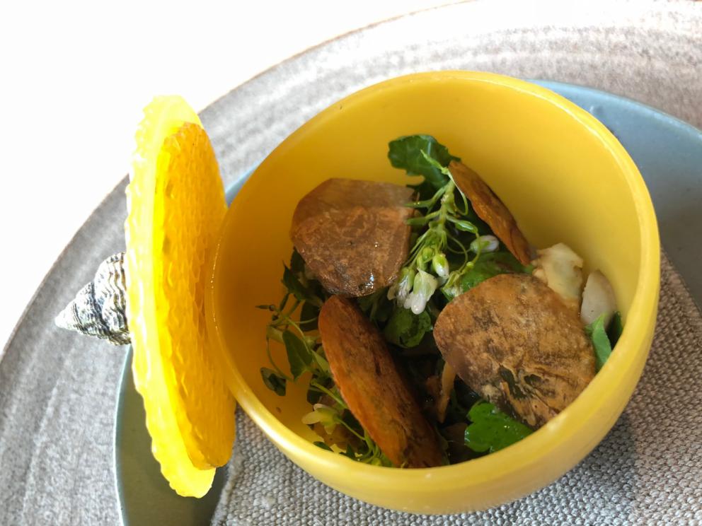 Photogallery






Noma 2.0 is in Christianshavn, the same neighbourhood as the first Noma. They’re 1.5 km apart, a 15 minutes’ walk. This picture shows the distance: to the right, there’s the warehouse of the old location (in Strandgade 93), to the left the smokestacks of Amager Bakke, the futuristic incinerator below which stands the new Noma (in Refshalevej 96)









Weather permitting, you can have a peaceful walk between the previous Noma to today’s Noma 









The new Noma is on an isthmus surrounded by canals. In the future they also want to reclaim some small parts for hydroponic farming









Bucolic scene with incinerator









Bikes left outside Noma. It’s the favourite means of transport among employees and interns









The long path taking you to the restaurant. The fence on the left shows how works are still in progress









On the two sides of the path there are the two new sections of the "Noma village", each with its specialty: grill, hot dishes, snacks, fermentations... In one month’s time, behind the fence we’ll have greenhouses, the test kitchen and the bread making area









To the left, before arriving at the restaurant, the future test kitchen. This will be run by Danish Mette Søberg with Riccardo Canella. "My first challenge?", reveals the latter, for a long time sous chef here, "is to work on the extraction of essential oils" 









The future Test Kitchen









The temporary gangway to the restaurant









Looking from the door to the restaurant, there’s a lake and the smokestacks puffing vapour from the Amager Bakke incinerator. It’s a futuristic project, both in terms of sustainability and architecture. It’s also known as Amager Slope or Copenhill, and its author is starchitect Bjarke Ingels, the same who designed the new Noma. Gradually opened in 2017, it transforms waste into electricity. The goal is to donate electricity to 62500 houses and hot water to 160000. It’s part of an ambitious project to transform Copenhagen into the first city in the world in terms of zero carbon dioxide emissions by 2025. By autumn this year, Amager Slope should open its ski slope, a climbing wall and a hiking track. You’ll be able to slalom on top of the incinerator









The windows from the dining room









Work is still in progress (photo taken on Thursday 22nd February 2018)









Traces of the old building, with barbwire. During WWII, they built bombs here









A view of the dining room at night (photo from Instagram/James Spreadbury)









The entrance to the restaurant









The usual ritual: a welcome from the entire staff, led by Rene Redzepi 









Behind the entrance, there are formaldehyde tanks with creatures from the abyss, shaped as in Damien Hirst’s works. The first image once you’re inside is to reproduce a Scandinavian village









The service kitchen is larger, more spacious and a completely open view from the dining room: "It’s the heart of our Scandinavian village", says Canella. There are 30 cooks working here now. 10 more, compared to the previous Noma









Large skylights above the cooks









There are currently more than 100 people working at Noma, of whom 63 are cooks - 26 employed, and 37 as interns









There’s fire in the kitchen, for the first time









On average, the dining room can host 40 people. "However", complains Redzepi, "there’s always someone who turns up with more people than the ones booked"









While the dining room is set, the outside space still need to be defined









The staff made the dining room decorations. There are no overly expensive designer objects









Dried fish









Seaweeds hanging from the ceiling









Dried octopus heads preserved in salt (with a balloon inside)














Bjarke Ingels and Redzepi’s plan included the wish to recreate a Danish farm









The luminous private dining room









The counter in the dining room. They drew the beams from the canals around the restaurant














The mise en place, bare and strictly without tablecloths









Water jug, candle, flower vase









A warm cloth, to begin with









Australian James Spreadbury, restaurant manager and partner at Noma









Welcome drink: Champagne extra brut Blanc d'Argile from Domaine Vouette et Sorbée









Sea Snail broth. The welcome dish at Noma is, as usual, a hot “soup”









Stefano Ferrano, from Torino, presents the following dish. There’s always a large Italian colony at Noma









Venus clams. Molluscs from Limfjord (Denmark) mixed with decorative clams, typical of Noma. Beside them, shells with blackcurrant oil and “Danish curry”, made with toasted coriander seeds, fennel and fennel seeds









The lid above the following dish. The mussels are not edible









Best of the mussel. Mussels open in a pan with water of fermented barley. «We recreate the mussel», says Canella, «using just the flaps, the best part». The paste is made with scraps from the mussel, cooked in smoked butter









The next dish is conceived and served by Riccardo Canella, the Paduan sous chef who conquered Redzepi, here with dining room intern Feline Hansen









Dried fruits and shrimps. In this case, the heads are not a decoration, but you must suck them –best not eat them because of the bones: they’re filled with a lovely prawn cream. The small crustaceans are still alive when they arrive on a ship straight from the Norwegian fjords









Inside, under the prawn broth skin, there’s fruits and vegetable preserved from the previous summer with raw prawns and gooseberry sauce with blackcurrant oil









How about beverages? There are three options, as usual: wine pairing (6 glasses plus a beer plus sake, 150 euros), juice pairing (juices and extracts, 110 euros) or a choice from the list. They recommend Champagne Chut... Libre from Val'Frison pour Dominique Derain, 50% Pinot Noir, 50% Chardonnay created by a couple who met at the old Noma. Well bodied, it will be a good match throughout the meal









As usual, the wine list starts with Champagne: the cheapest is 1400 crowns (190 euros)









White wines begin with labels from cold climates: first Austria, increasingly popular for its natural wines, then Germany, then all the others









How about Italy? Few names, among the white wines, from North and South









A dozen red/orange wines









Sea star, that is to say Cured trout roe and eggs, the emblem dish of this new era. They recommend moving the teaspoon from the heart to the edges of the tentacles. Aesthetics win over taste









Jellyfish. The jellyfish gel in the middle is in fact a clarified broth of calamari and recalls the texture of jellyfish. "We tried to cook jellyfish in 300 different ways but none was convincing so far". All around, pickled seaweed. The gel is almost tasteless, it serves to clean the palate after the pickles









Rene Redzepi himself presents the content of the first Seafood platter.









French style service with a small plate below for the empty shells









It’s made of two (per two) pieces: queen clam and mahogany clam









The Queen Clam is a very small variety of Norwegian scallop, seasoned with a vegetal reduction made with cucumber and peas miso. The red tip is the coral. "You should eat it using the top shell ", recommends Redzepi









The Mahogany clam is a centennial clam from the North Sea, very popular in Denmark and Iceland. «You can tell the age by the number of rings, like with trees», says Redzepi, «In 2007 they found one that was 450 years old. We’ve had it in the menu for a decade or so». The razor clam shell serves as teaspoon









Inside, there’s obviously not just a bare Mahogany. «We open it when the client arrives», says Canella, «remove the entrails and then slice it so as to preserve its firm texture». It’s seasoned with stir-fried gooseberry, capers of blackcurrants and blackcurrant sprouts preserved in vinegar. The sauce is made with mussel water









A note on the chairs: they’re more minimalistic. They’re no longer covered in sheepskin or leather from other Danish animals, in the style of Noma 1.0. The most significant element is the napkin: if you go to the toilet, they no longer replace it with a new one. There’s the old one, tied to the chair. "This is sustainability", they explain









The second seafood platter. It’s made of Sea cucumber and sour cream in various textures, including «chicharrones» (at 9 o’clock), sea urchins (at 12 and 3) and gigas oyster (at 6)









Sea urchins pressed in fresh cream and pumpkin seeds









Giga Oyster, a huge oyster from the Pacific, quickly steamed and garnished with pickles. Noma only reserved one thousand of these. In the menu until available









The following dish, off the menu, is again from Canella: horse mussel ragout, rare specimen of which 30 arrive at 'Noma each week









They cook the mussel as if it were kidney, in a sort of Bolognese sauce but with ginger. Ginger? "Yes, we’ve decided to include it, as with other spices, after our Mexican experience"









Another Italian presents a dish, Edoardo Fiaschi from Prato, at Noma for 3 years now









Squid in seaweed butter. An almost neglected Danish squid lightly seared in fermented koji oil, rolled and seasoned with seaweed butter and served on sticks of blackcurrant that widen its aromas. Formidable and beautiful









The following dish is inside a nice bee wax container. It’s made with balloons covered multiple times in bee wax. «We spent weeks making them. We’ve made thousands». They’re disposable...






