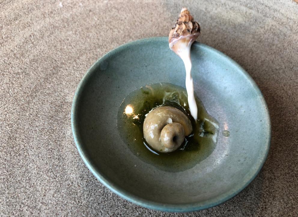 Photogallery






Noma 2.0 is in Christianshavn, the same neighbourhood as the first Noma. They’re 1.5 km apart, a 15 minutes’ walk. This picture shows the distance: to the right, there’s the warehouse of the old location (in Strandgade 93), to the left the smokestacks of Amager Bakke, the futuristic incinerator below which stands the new Noma (in Refshalevej 96)









Weather permitting, you can have a peaceful walk between the previous Noma to today’s Noma 









The new Noma is on an isthmus surrounded by canals. In the future they also want to reclaim some small parts for hydroponic farming









Bucolic scene with incinerator









Bikes left outside Noma. It’s the favourite means of transport among employees and interns









The long path taking you to the restaurant. The fence on the left shows how works are still in progress









On the two sides of the path there are the two new sections of the "Noma village", each with its specialty: grill, hot dishes, snacks, fermentations... In one month’s time, behind the fence we’ll have greenhouses, the test kitchen and the bread making area









To the left, before arriving at the restaurant, the future test kitchen. This will be run by Danish Mette Søberg with Riccardo Canella. "My first challenge?", reveals the latter, for a long time sous chef here, "is to work on the extraction of essential oils" 









The future Test Kitchen









The temporary gangway to the restaurant









Looking from the door to the restaurant, there’s a lake and the smokestacks puffing vapour from the Amager Bakke incinerator. It’s a futuristic project, both in terms of sustainability and architecture. It’s also known as Amager Slope or Copenhill, and its author is starchitect Bjarke Ingels, the same who designed the new Noma. Gradually opened in 2017, it transforms waste into electricity. The goal is to donate electricity to 62500 houses and hot water to 160000. It’s part of an ambitious project to transform Copenhagen into the first city in the world in terms of zero carbon dioxide emissions by 2025. By autumn this year, Amager Slope should open its ski slope, a climbing wall and a hiking track. You’ll be able to slalom on top of the incinerator









The windows from the dining room









Work is still in progress (photo taken on Thursday 22nd February 2018)









Traces of the old building, with barbwire. During WWII, they built bombs here









A view of the dining room at night (photo from Instagram/James Spreadbury)









The entrance to the restaurant









The usual ritual: a welcome from the entire staff, led by Rene Redzepi 









Behind the entrance, there are formaldehyde tanks with creatures from the abyss, shaped as in Damien Hirst’s works. The first image once you’re inside is to reproduce a Scandinavian village









The service kitchen is larger, more spacious and a completely open view from the dining room: "It’s the heart of our Scandinavian village", says Canella. There are 30 cooks working here now. 10 more, compared to the previous Noma









Large skylights above the cooks









There are currently more than 100 people working at Noma, of whom 63 are cooks - 26 employed, and 37 as interns









There’s fire in the kitchen, for the first time









On average, the dining room can host 40 people. "However", complains Redzepi, "there’s always someone who turns up with more people than the ones booked"









While the dining room is set, the outside space still need to be defined









The staff made the dining room decorations. There are no overly expensive designer objects









Dried fish









Seaweeds hanging from the ceiling









Dried octopus heads preserved in salt (with a balloon inside)














Bjarke Ingels and Redzepi’s plan included the wish to recreate a Danish farm









The luminous private dining room









The counter in the dining room. They drew the beams from the canals around the restaurant














The mise en place, bare and strictly without tablecloths









Water jug, candle, flower vase









A warm cloth, to begin with









Australian James Spreadbury, restaurant manager and partner at Noma









Welcome drink: Champagne extra brut Blanc d'Argile from Domaine Vouette et Sorbée









Sea Snail broth. The welcome dish at Noma is, as usual, a hot “soup”









Stefano Ferrano, from Torino, presents the following dish. There’s always a large Italian colony at Noma









Venus clams. Molluscs from Limfjord (Denmark) mixed with decorative clams, typical of Noma. Beside them, shells with blackcurrant oil and “Danish curry”, made with toasted coriander seeds, fennel and fennel seeds









The lid above the following dish. The mussels are not edible









Best of the mussel. Mussels open in a pan with water of fermented barley. «We recreate the mussel», says Canella, «using just the flaps, the best part». The paste is made with scraps from the mussel, cooked in smoked butter









The next dish is conceived and served by Riccardo Canella, the Paduan sous chef who conquered Redzepi, here with dining room intern Feline Hansen









Dried fruits and shrimps. In this case, the heads are not a decoration, but you must suck them –best not eat them because of the bones: they’re filled with a lovely prawn cream. The small crustaceans are still alive when they arrive on a ship straight from the Norwegian fjords









Inside, under the prawn broth skin, there’s fruits and vegetable preserved from the previous summer with raw prawns and gooseberry sauce with blackcurrant oil









How about beverages? There are three options, as usual: wine pairing (6 glasses plus a beer plus sake, 150 euros), juice pairing (juices and extracts, 110 euros) or a choice from the list. They recommend Champagne Chut... Libre from Val'Frison pour Dominique Derain, 50% Pinot Noir, 50% Chardonnay created by a couple who met at the old Noma. Well bodied, it will be a good match throughout the meal









As usual, the wine list starts with Champagne: the cheapest is 1400 crowns (190 euros)









White wines begin with labels from cold climates: first Austria, increasingly popular for its natural wines, then Germany, then all the others









How about Italy? Few names, among the white wines, from North and South









A dozen red/orange wines









Sea star, that is to say Cured trout roe and eggs, the emblem dish of this new era. They recommend moving the teaspoon from the heart to the edges of the tentacles. Aesthetics win over taste









Jellyfish. The jellyfish gel in the middle is in fact a clarified broth of calamari and recalls the texture of jellyfish. "We tried to cook jellyfish in 300 different ways but none was convincing so far". All around, pickled seaweed. The gel is almost tasteless, it serves to clean the palate after the pickles









Rene Redzepi himself presents the content of the first Seafood platter.









French style service with a small plate below for the empty shells









It’s made of two (per two) pieces: queen clam and mahogany clam









The Queen Clam is a very small variety of Norwegian scallop, seasoned with a vegetal reduction made with cucumber and peas miso. The red tip is the coral. "You should eat it using the top shell ", recommends Redzepi









The Mahogany clam is a centennial clam from the North Sea, very popular in Denmark and Iceland. «You can tell the age by the number of rings, like with trees», says Redzepi, «In 2007 they found one that was 450 years old. We’ve had it in the menu for a decade or so». The razor clam shell serves as teaspoon









Inside, there’s obviously not just a bare Mahogany. «We open it when the client arrives», says Canella, «remove the entrails and then slice it so as to preserve its firm texture». It’s seasoned with stir-fried gooseberry, capers of blackcurrants and blackcurrant sprouts preserved in vinegar. The sauce is made with mussel water









A note on the chairs: they’re more minimalistic. They’re no longer covered in sheepskin or leather from other Danish animals, in the style of Noma 1.0. The most significant element is the napkin: if you go to the toilet, they no longer replace it with a new one. There’s the old one, tied to the chair. "This is sustainability", they explain









The second seafood platter. It’s made of Sea cucumber and sour cream in various textures, including «chicharrones» (at 9 o’clock), sea urchins (at 12 and 3) and gigas oyster (at 6)









Sea urchins pressed in fresh cream and pumpkin seeds









Giga Oyster, a huge oyster from the Pacific, quickly steamed and garnished with pickles. Noma only reserved one thousand of these. In the menu until available









The following dish, off the menu, is again from Canella: horse mussel ragout, rare specimen of which 30 arrive at 'Noma each week









They cook the mussel as if it were kidney, in a sort of Bolognese sauce but with ginger. Ginger? "Yes, we’ve decided to include it, as with other spices, after our Mexican experience"









Another Italian presents a dish, Edoardo Fiaschi from Prato, at Noma for 3 years now









Squid in seaweed butter. An almost neglected Danish squid lightly seared in fermented koji oil, rolled and seasoned with seaweed butter and served on sticks of blackcurrant that widen its aromas. Formidable and beautiful









The following dish is inside a nice bee wax container. It’s made with balloons covered multiple times in bee wax. «We spent weeks making them. We’ve made thousands». They’re disposable...









Sea snail and roses. They recommend to: "Eat it keeping the bee wax on your hands "






