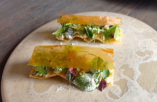 Galleria fotografica






In cammino verso il Noma. Il ristorante è al piano terra del palazzone più a sinistra. Per arrivarci dalla popolare insenatura di Nyhavn (il punto da cui è scattata la foto), occorre fare un bel giro. Ma si notano i lavori per la costruzione di un ponte. Che condurrà dritto all'insegna








Altra prospettiva sul Noma da Nyhavn. Il ristorante galleggia sulla Christianshavn, una delle tante isole artificiali che compongono Copenhagen








Di là del fiume, sulla lunga via che conduce allo spiazzo del Noma








Uno scenario molto tranquillo, di case pastello. Il silenzio è perché vanno tutti in bici













Al massimo si sente rombare qualche scafo








Il vascello davanti al Noma. Oltre a quella danese, sventolano le bandiere di Isole Far Oer e Groenlandia: le loro ambasciate sono nello stesso palazzo del ristorante. Coerenza nordica








Il retro del ristorante. L'80% delle 80 persone che lavorano al Noma viene a lavorare in bici, chef incluso








Dietro al ristorante, un'iscrizione ricorda i passeggeri scomparsi a bordo della danese Hans Hedtoft. Il transatlantico si scontrò il 30 gennaio 1959 contrò un iceberg in Groenlandia. Fu ritrovata solo una cintura di sicurezza
 








L'ingresso del ristorante, al civico 93 di Strandgade








La vista, ingresso alle spalle








Tra l'ingresso e la cucina a vista, spicca un corner di decoro simil-giapponese. A sinistra s'intravede Noma, time and place in Nordic Cuisine, edizioni Phaidon, un testo fondamentale per approfondire tutti i rivoli del Redzepi-mondo. La versione italiana si ordina qui








Una pianta di piccoli agrumi orla la cucina a vista








La porta d'ingresso vista dalla cucina








Le sedie, molto comode, sono anni Sessanta con schienali foderati di pelle di pecora, alcune più morbide di altre








I tavoli sono ampi e senza tovaglie. Attorno prevale il grigio e i colori rustici, sulle travi in legno del soffitto ma anche sulle divise dei ragazzi di sala








La finestra accanto al nostro tavolo








E' lo chef Rene Redzepi a introdurci al pasto: in un vaso di fiori danesi, l'unico pendaglio commestibile è una sorta di carta musica croccante (flatbread) di farina di malto all'aroma di ginepro. Nel piattino in basso, una deliziosa crème fraîche acida per intingerlo








Il flatbread è quello che svetta. "Ma se ci tenete, provate a mangiare anche i fiori", scherza Redzepi. Il cuoco scompare nelle segrete del Noma. Lo ritroveremo solo alla fine del pasto








Tutti i 14 appetizer si mangeranno con le mani. Unica posata, il coltello per tirar su e leccare la crème fraîche da sola (da fare quando tutti gli altri clienti son distratti, però)








Moss and Cep: Muschio di renna con polvere di funghi porcini. E' il corpo bianco, molto saporito ed evanescente, da intingere anch'esso nella crème fraîche
 








Crispy pork skin and black currant: Pelle di maiale croccante e ribes nero, lo strato più esterno. Aspro e croccante








Il ribes nero non ci lascerà prima di molto tempo








Blue mussels and celery: cozze e sedano. Solo due sono quelle buone








La parte inferiore del guscio è commestibile (ancora farina di malto)








Il quinto appetizer è nascosto in una deliziosa scatola di biscotti in latta della tradizione danese (chi non ricorda i Danish butter cookies?)








Cinque tondini, ma solo due "interessanti"








Si chiamano Cheese cookies, rocket and stems, letteralmente Biscotti al formaggio, ruchetta e gambi di erbe aromatiche, un felice snack potenzialmente riproducibile nei nord e nei sud del mondo








Appetizer #6: Potato and duck liver, Patate e fegato d'anatra: le patate croccanti sono in due strati e a mo' di sandwich racchiudono la mousse di fegato. La spolverata è di funghi trombette dei morti, disidratati e polverizzati, una tecnica che troveremo frequentemente








Dried carrot and sorrel, Carote grigliate a fuoco lento per 14 ore, disidratate e servite su polvere di fieno. Si intingono nell'emulsione di acetosella accanto. Un grande piatto perché di inattesa, energica acidità








Ottava entrée: Caramelized milk and cod liver, Biscotto di latte caramellato e fegato di merluzzo, quest'ultimo ghiacciato e pulito. Il secondo dona un aroma molto strong, che domina sul biscotto croccante. Per palati muscolari








Le uova dentro l'uovo








Pickled and smoked quails eggs, Uova di quaglia sbollentate, marinate e affumicate, un classico del Noma. Il tuorlo è completamente liquido








Col Veal fibres and söl, Filamenti di vitello e söl, decimo appetizer, entra in gioco per la prima volta un'alga di mare. E' il söl, appunto, dulse in inglese, Palmaria palmata nella tassonomia scientifica, un'alga rossa incastrata nei filamenti di vitello precedentemente tagliati sottili e poi fritti. Curioso l'impiatto a nido di ingredienti che alla fine incastrano terra e mare





