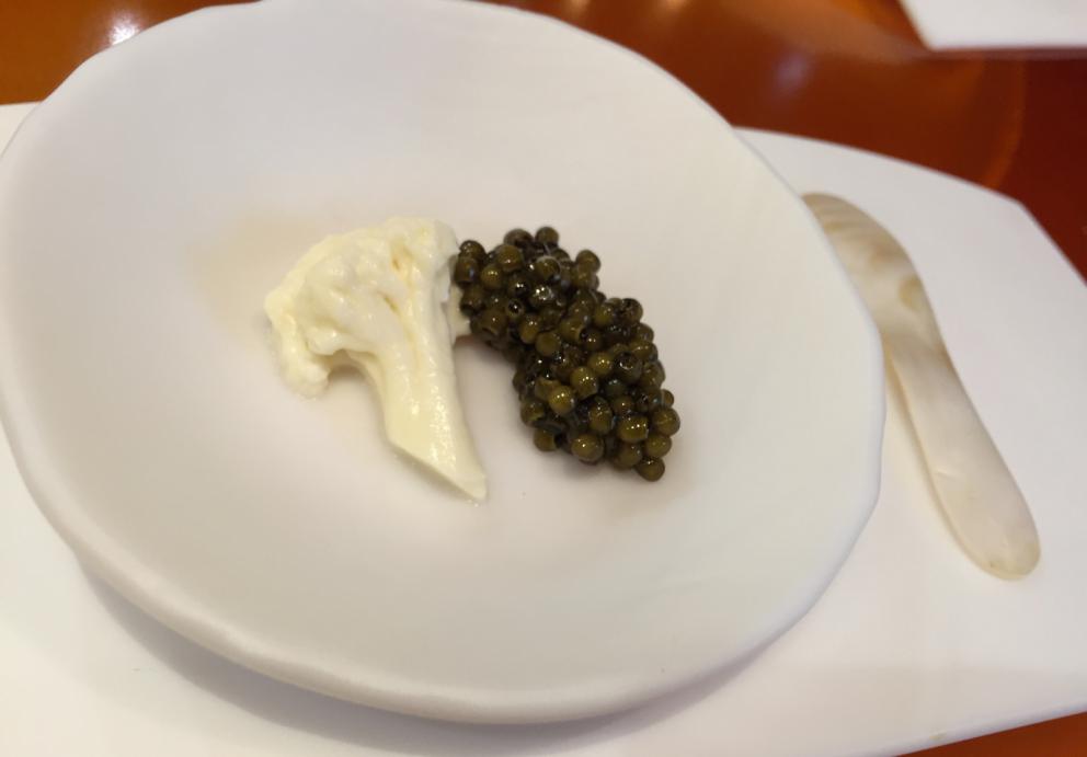 Galleria fotografica






Consommè de garbanzos. Prima che cominci il menu degustazione, viene portata al tavolo una bottiglia di vetro contenente del brodo freddo di ceci (in alto a destra). Ventitrè piatti dopo, alla fine del percorso "salato", verrà versato, in un bicchierino da grappa, del brodo caldo di jamon iberico da una teiera. Sopra ancora, la schiuma del brodo di ceci. Un caldo-freddo speciale (foto @ticketsbar instagram)









Tosta de pollo y anchoa. Primo piatto: toast di pelle di pollo con lisca di acciuga. A lato, una crema di acciughe composta da burro e pasta di acciughe









Olive Gordal. Uno dei simboli della saga Adrià: le olive sono immerse in un liquido d'olio extravergine d'oliva, cannella, buccia di limone e anice stellato. Si tirano su con un cucchiaino forato, si poggiano su una conchiglia di legno a lato e da qui in bocca. Gordal è una varietà dall'Andalusia









Prima preparazione rifinita al tavolo: Polo de almendras









Polo de almendras è uno stecco di gelato al latte di mandorle, spennellato sul posto con olio d'oliva e cosparso con granelle di mandorle, fiori di sambuco e sale. E' servito su un piatto con cubetti di ghiaccio. Dolce(salato) e gelato all'inizio del pasto e non alla fine, uno schema molto Adrià






