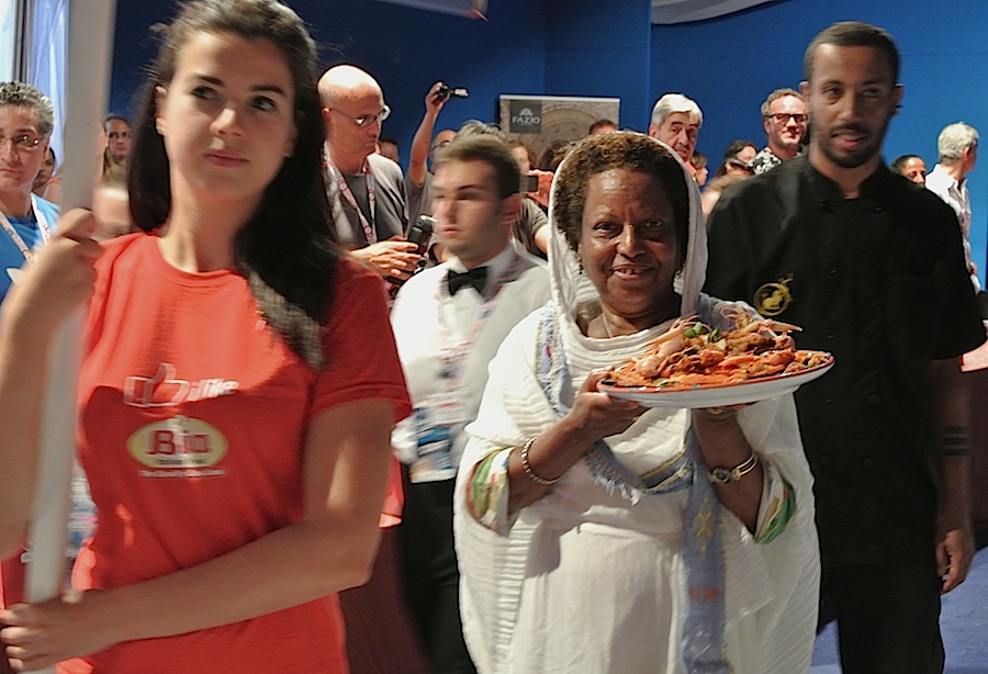 Galleria fotograficaIl cannolo di cous cous di Enrico Panero, del ristorante Da Vinci a Eataly Firenze, usato come evidenziatorePrima nazione in gara al Cous Cous Fest 2014 il Marocco con Majda Nabaoui, cuoca 19enne in forza all'Osteria Francescana a ModenaMajda Nabaoui, in Italia, a Modena, dall'et&agrave; di 9 anni, ha chiamato la sua proposta Da Modena al Marocco passando per la Sicilia, la sua colazione la mattina di sabatoI due concorrenti della Tunisia, entrambi in forza al Taglio a Milano, a destra Domenico della Salandra e al centro Mohamed Mabrouk catturato dalla bellezza della presentatrice Eliana ChiavettaL'Arancino di cous cous grazie al quale la Tunisia &egrave; arrivata alla finale a livello di giuria popolare superando il Marocco per appena un centesimo: 8,92 contro 8,91. Al suo interno scampi freschi. Nota curiosa: visto che eravano nel Trapanese, quindi Sicilia occidentale, sarebbe stato pi&ugrave; corretto chiamare il piatto ArancinaTre giorni di assaggi, tutto nel PalaBia, il tendone ridosso della spiaggia di San Vito Lo Capo. Il cielo ti invitava a mollare tutto e a tuffartiIl Cous Cous dolce, nome concreto del piatto della Francia, delle cuoche Marion Roger (cous chef di Alice Delcourt all'Erba Brusca a Milano) e Chiara Cilio, che hanno proposto un uso insolito del cous cous, in forma dolce, con tanto di gelato alla verbena. Con questo dessert, la Roger ha vinto il premio per l'originalit&agrave; e sfiorato il successo assoluto, centrato dalla Delcourt nel 2011 e 2012Maziar Farivar, radici iraniane e cittadinanza statunitense. Del suo piatto ricorderemo solo un eccessivo e gratuito uso del peperoncino. Doveva essere un cous cous nel segno dello Shrimp Jambalya ma, eliminato il prosciutto affumicato nel timore di imbattersi in musulmani in giuria, tutto &egrave; crollato.Il cous cous americano, un piatto imbarazzante, facile preferirgli quello francese. La giuria popolare ha votato il dessert 8,86 e il cous cous patriottico 7,86 (ma la giuria di esperti &egrave; stata ancora pi&ugrave; severa)Mohamed Mabrouk e Domenico della Salandra per una volta schierati nella giuria popolareIsraele in gara contro il Libano grazie a Michael Korenman, tutti presi in contropiede perch&eacute; si aspettavano un Michele, un lui e non una leiMichael Korenman &egrave; stata anche la cuica personale di Oprah Winfrey in America, conduttrice tiv&ugrave; e attrice. Il suo cous cous &egrave; piaciuto pi&ugrave; agli esperti che al pubblico. Ricco di spunti come i falafel, ottimi i singoli pezzi meno l'assemblaggio finale e un attimo inutile il tonno come nota del mare. Il piatto non aveva un nome: "Abbiamo avuto un'estata difficile per via della guerra che proprio non avevo pensato a come chiamarlo. Lo faccio ora e lo chiamo PACE". Applausi scrosciantiNahida Salman, cuoca libanese che dal 2006 vive a Ragusa in Sicilia, tra i suoi parenti anche l'attuale presidente della Repubblica del Libano Michel Suleiman. Il suo cous cous, lo Yakneh Tabule alla carne di agnello, &egrave; stato preferito per due centesimi dalla giuria popolare: 8,57 contro 8,55.Un dettaglio del cous cous libanese, il tabul&egrave; usato dalla chef come ripieno degli involtini di foglie di viteCome per Israele, la partecipazione dei cuochi della Palestina assume sempre un significato che trascende quello gastronomico. A volte ci scappa pure un signor piatto, non &egrave; stata questa la volta ma Hani Kasabra e Odeh Abu El Hawa hanno lo stesso strappato applausi. Se &egrave; stata un'estate pesante per chi vive in Israele, figuriamoci per loro (che, comunque, non arrivano da Gaza bensi da Betlemme). Sono ampiamente scusati se non hanno versato il miele in un cous cous di pollo e verdure in brodo, miele annunciato nel nome stesso della preparazione.Il Cous Cous con pollo e verdure della Palestina. Tanta buona volont&agrave;.Mamma Africa alias Konate Abibata, nativa di Abidjian e a Palermo dal 1994 dove presto avrebbe aperto un'osteria nel quartiere di Santa Chiara per i suoi connazionali ivoriani e via via per sempre pi&ugrave; italiani. Gi&agrave; nonna di sette nipoti, anima una fondazione a favore dei bambini del Burkina Faso, "un Paese ancora pi&ugrave; povero della Costa d'Avorio". Vincitrice due volte del Cous Cous Fest, 2006 e 2008, superata la Palestina per 9,11 contro 8,24, Mamma Africa si &egrave; aggiudicata il premio per la migliore presentazione.Mamma Africa ha chimato il suo cous cous Gli spiedini della nonna, lei ormai nonna e molto attaccata a sua madre. Per&ograve; gli spiedini di manzo non hanno sfilato. La cuoca ivoriana ha usato l'occasione per lanciare un messaggio di pace e di fratellanza tra le nazioni di Africa (la mano nera) e Europa (il fondo bianco) nel segno di un cuoro rosso e vivo. Il cous cous della Costa d'Avorio come &egrave; stato servito alla giuria tencica. Particolarmente scomodo e brutto il bicchiere per il sugo di carne, ma molto funzionale alla riuscita del piatto perch&eacute; uno poteva versarlo subito prima di papparselo. In finale invece Mamma Africa ha preferito, in assenza di bricchetti, versare il sugo prima di servire, ma cos&igrave; il torrino &egrave; risultato asciutto.L'ultimo confronto eliminatorio ha visto in gara l'Italia e l'Eritrea. Primi a uscire in sala i cuochi azzurri, il sanvitese Giuseppe Salmeri, in forza all'hotel Capo San Vito, tutto a sinistra nella foto, e il milanese Andrea Provenzani, chef-patron del Liberty.Andrea Provenzani aveva vinto le selezioni di giugno per rappresentare l'Italia al Cous Cous Fest vero e proprio, assieme con Giuseppe Salmeri, grazie a un piatto dominato dal pesce spada. Tre mesi dopo la ricciola, un esemplare di 36 chili, ha preso il posto dello spada e il piatto, presentato come La mia Sicilia, &egrave; diventato La nostra Sicilia, di Andrea e di Giuseppe. A fine eleminatorie, &egrave; risultato il pi&ugrave; voitato: 9,44. A farne le spese l'Eritrea, voto 8,58.Al cous cous italiano, per essere gustato, mancava il tocco finale, un latte di mandorle naturale, preparato dagli stessi chef.