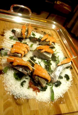 Galleria fotograficaSpugne di pane aromatizzate
Dopo il consueto pre-appetizer delle verdure disidratate (primo contenitore), arrivano le spugne, seconda parentesi colorata che rallegra il pasto dall&rsquo;inizio. In questo caso sono aromatizzate agli spinaci e uova di salmone; alla cipolla cotta al forno con terrina di vitello e alla curcuma con lardo. &laquo;Ma le combinazioni possono essere infinite&raquo;, spiega Matteo Baronetto, braccio destro di Carlo Cracco, &laquo;si possono utilizzare anche in pasticceria al cocco, ai lamponi&hellip; La tecnica &egrave; mutuata da Ferran Adri&agrave;. Abbiamo cercato di personalizzarla nel gusto. A me ricordano molto i canap&egrave; della tradizione piemontese. Senza maionese naturalmente&raquo;. Vivacit&agrave; cromatica ulteriormente ravvivata da un terzo contenitore di foglie di shiso e fiori di zucchina in tempura con riso venere e riso ai piselli fritto (che non vedete perch&eacute;, ahinoi, la foto &egrave; venuta male)Lamponi e sambuco
Nella girandola di appetizer spiccano questi piccoli lamponi farciti con infusione di sambuco serviti sul ghiaccio. &laquo;I suoi fiori in questi giorni li senti anche a Milano, passeggiando al parco. Un odore forte e piacevole. Stiamo lavorando allo stesso concetto anche con le fragole, i mirtilli, il ribes o i gelsi. Un'idea che interpreta quella tradizione sudamericana che ribalta l'ordine delle pietanze, con la frutta all'inizio del percorso, un po' come gi&agrave; succede con la nostra insalata russa caramellata. Sposa nota fruttate e speziate. Ma al posto della frutta potrebbe starci benissimo un'oliva, perch&eacute; no?&raquo;Panino al seitan con insalata e tartufo nero
Un panino di seitan dal contenuto variabile: al congresso di Identit&agrave; Milano 2012, sede della sua anteprima, c&rsquo;erano songino, fiori di piselli e lingua. &laquo;Sono masse di seitan da 15 grammi messe a cuocere nel micro-onde a 90 watt. Il calore fa lievitare il glutine tipo quasi alla maniera del vetro soffiato. L&rsquo;ispirazione ci &egrave; venuta da una ricetta di Simone Salvini letta sul sito di Identit&agrave; Golose&raquo;. A Milano la lingua cancell&ograve; l&rsquo;apparente connotazione vegana del piattoOstriche, crema di piselli e menta
&laquo;Ostriche con semplice crema leggera di latte e piselli messa nel sifone. Combina lo iodato dell&rsquo;ostrica, la dolcezza dei piselli e la freschezza dei menta. La puoi aggiungere anche sui tartufi di mare&raquo;Uovo di quaglia affumicato al rosmarino e prezzemolo bollito
&laquo;L&rsquo;uovo di quaglia viene bollito e pelato. Il tuorlo &egrave; laccato con gelatina di latte ai capperi. Le due met&agrave; dell&rsquo;albume sono arricchite con crema leggera di prezzemolo bollito. C&rsquo;&egrave; una nota affumicata al rosmarino, che gli diamo prima di farcire. &Egrave; un piatto che ricorda un po&rsquo; le uova sode ripiene&raquo;. Giusto il ricordoFoglie di shiso rosse e verdi con gambero e melassa di cipolla
&laquo;Un gambero (ligure, e quindi pi&ugrave; piccolo di quelli pescati in Sicilia) viene posto tra due foglie di shiso a carpaccio, tagliato e tenuto in frigo per 8 ore in modo che gli elementi si compenetrino d&rsquo;aromi l&rsquo;un l&rsquo;altro. La melassa &egrave; ottenuta invece stracuocendo in forno la cipolla, che si addenser&agrave; sfruttando i suoi zuccheri naturali. Completa l&rsquo;opera il nero hawaiano, un sale minerale, vulcanico. E un tocco di burro fuso per aiutare la balsamicit&agrave; dello shiso a esprimersi&raquo;Orata cotta appena su croccante di nocciole
&laquo;Il croccante viene messo in forno per 3 minuti. Tirato fuori, gli si poggia sopra il sashimi di orata, che 'cuocer&agrave;' cos&igrave; acquisendo la nota dolce dell'olio naturale del croccante&raquo;. Una sorta di sashimi alla piemontese. Vietato mangiare il croccantino sottostante perch&eacute; altrimenti l'orata non si sente. Semmai dopo...Salmone marinato e foie gras
Piatto in carta da Cracco pi&ugrave; o meno da un anno, &egrave; un inno all&rsquo;opulenza e alle note grasse. &laquo;Volevamo dare una variante allo stra-classico salmone col burro spalmato sul crostino&raquo;, spiega Baronetto.&nbsp;Il boccone del salmone senza foie gras deve rimanere per ultimo &laquo;senn&ograve; l&rsquo;avremmo chiamato foie gras e salmone&raquo;Gamberi, nocciole cotte e sambuco
La fonte d'ispirazione c'&egrave; ma proprio non si vede: &egrave; la celebre passatina di ceci con gamberi di Fulvio Pierangelini.&nbsp;&laquo;Casualmente ci siamo accorti che la nocciole, se bollite e messe per breve tempo in forno, prendono la consistenza dei ceci, o comunque di un legume&raquo;. L'ulteriore nota distintiva dal masterpiece pierangeliniano sono il sambuco e le foglie di rucola: &laquo;danno una nota agliacea e leggermente piccante che a me piace molto&raquo;Lattume, fagiolini, acetosella
Un piatto all'apparenza hardcore (il lattume &egrave; lo sperma delle gonadi del tonno maschio), stemperato dalla presenza di foglie di acetosella e da fagiolini liguri pelandroni, specie molto pi&ugrave; tenera delle taccole.&nbsp;&laquo;Li abbiamo cotti nel t&egrave; Lapsang Souchong per dare loro una nota affumicata. Questo aiuta a lenire il sapore densissimo del lattume, appena scottato. Per certi versi questo piatto mi ricorda un po' il filone di vitello piemontese, col midollo della spina dorsale. E' un modo per valorizzare una primizia, il lattume, che in queste settimane, coi tonni che invadono il Medterraneo a scopo riproduttivo, &egrave; fantastico&raquo;Tagliolini di farina di grano arso con salsiccia cruda e salsa al rafano
Ci torneremo presto nella newsletter Identit&agrave; di PastaSpugnole, ricci e cous cous di amaranto
&laquo;Il cous cous &egrave; quasi crudo e sabbioso, una consistenza che serve ad arricchire lo spettro di consistenze dei ricci e delle spugnole, molto cotti&raquo;. Un piatto di grande assonanze minerali, terragneLa Milanese sbagliata
Piatto presentato a Identit&agrave; Milano 2012, ironizza sulle pessime &ldquo;orecchie di elefante&rdquo; cucinate espresse e precotte in tante insegne, milanesi e non. Spesso, infatti, l&rsquo;impanatura si stacca dalla carne, che ci &ldquo;balla&rdquo; dentro. Nella versione Cracco-Baronetto le due componenti sono direttamente separate: &laquo;L&rsquo;impanatura la facciamo a parte nell&rsquo;uovo sbattuto e poi la cuciamo in un foglio di carta da forno nel burro chiarificato. Il carpaccio &egrave; di vitello, crudo alla maniera delle peggiori versioni. Sopra ci grattugiamo della buccia di limone&raquo;. Un errore riuscitissimo
Guancia di vitello brasata con cumino tostato
Carne tenerissima, sotto&rsquo;olio e cotta sottovuoto. &laquo;E' carne brasata alla maniera classica, ma senza il vino. La serviamo spezzata con le mani e cosparsa di cumino prima tostato e triturato&raquo;Gamberi al carbone 1
Il nuovo&nbsp;ma&icirc;tre del Ristorante&nbsp;Cracco, Francesco Palumbo osserva il vassoio di spiedini di gamberi cotti sul carbone ardente, altro piatto presentato a Identit&agrave; Milano 2012. Nelle intenzione degli autori, sfrutta le tradizioni conviviali del Nord Europa e della Grecia:&nbsp;&laquo;Il carbone &egrave; selezionato da un produttore francese, l'unico a non trattarlo col benzene. Al posto dei gamberi, piccoli perch&eacute; piccoli sono i tizzoni, potrebbero benissimo starci scampi, capesante. O anche dei piccoli bocconcini di pollo&raquo;