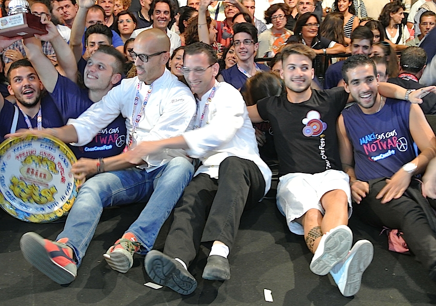 Galleria fotograficaIl cannolo di cous cous di Enrico Panero, del ristorante Da Vinci a Eataly Firenze, usato come evidenziatorePrima nazione in gara al Cous Cous Fest 2014 il Marocco con Majda Nabaoui, cuoca 19enne in forza all'Osteria Francescana a ModenaMajda Nabaoui, in Italia, a Modena, dall'et&agrave; di 9 anni, ha chiamato la sua proposta Da Modena al Marocco passando per la Sicilia, la sua colazione la mattina di sabatoI due concorrenti della Tunisia, entrambi in forza al Taglio a Milano, a destra Domenico della Salandra e al centro Mohamed Mabrouk catturato dalla bellezza della presentatrice Eliana ChiavettaL'Arancino di cous cous grazie al quale la Tunisia &egrave; arrivata alla finale a livello di giuria popolare superando il Marocco per appena un centesimo: 8,92 contro 8,91. Al suo interno scampi freschi. Nota curiosa: visto che eravano nel Trapanese, quindi Sicilia occidentale, sarebbe stato pi&ugrave; corretto chiamare il piatto ArancinaTre giorni di assaggi, tutto nel PalaBia, il tendone ridosso della spiaggia di San Vito Lo Capo. Il cielo ti invitava a mollare tutto e a tuffartiIl Cous Cous dolce, nome concreto del piatto della Francia, delle cuoche Marion Roger (cous chef di Alice Delcourt all'Erba Brusca a Milano) e Chiara Cilio, che hanno proposto un uso insolito del cous cous, in forma dolce, con tanto di gelato alla verbena. Con questo dessert, la Roger ha vinto il premio per l'originalit&agrave; e sfiorato il successo assoluto, centrato dalla Delcourt nel 2011 e 2012Maziar Farivar, radici iraniane e cittadinanza statunitense. Del suo piatto ricorderemo solo un eccessivo e gratuito uso del peperoncino. Doveva essere un cous cous nel segno dello Shrimp Jambalya ma, eliminato il prosciutto affumicato nel timore di imbattersi in musulmani in giuria, tutto &egrave; crollato.Il cous cous americano, un piatto imbarazzante, facile preferirgli quello francese. La giuria popolare ha votato il dessert 8,86 e il cous cous patriottico 7,86 (ma la giuria di esperti &egrave; stata ancora pi&ugrave; severa)Mohamed Mabrouk e Domenico della Salandra per una volta schierati nella giuria popolareIsraele in gara contro il Libano grazie a Michael Korenman, tutti presi in contropiede perch&eacute; si aspettavano un Michele, un lui e non una leiMichael Korenman &egrave; stata anche la cuica personale di Oprah Winfrey in America, conduttrice tiv&ugrave; e attrice. Il suo cous cous &egrave; piaciuto pi&ugrave; agli esperti che al pubblico. Ricco di spunti come i falafel, ottimi i singoli pezzi meno l'assemblaggio finale e un attimo inutile il tonno come nota del mare. Il piatto non aveva un nome: "Abbiamo avuto un'estata difficile per via della guerra che proprio non avevo pensato a come chiamarlo. Lo faccio ora e lo chiamo PACE". Applausi scrosciantiNahida Salman, cuoca libanese che dal 2006 vive a Ragusa in Sicilia, tra i suoi parenti anche l'attuale presidente della Repubblica del Libano Michel Suleiman. Il suo cous cous, lo Yakneh Tabule alla carne di agnello, &egrave; stato preferito per due centesimi dalla giuria popolare: 8,57 contro 8,55.Un dettaglio del cous cous libanese, il tabul&egrave; usato dalla chef come ripieno degli involtini di foglie di viteCome per Israele, la partecipazione dei cuochi della Palestina assume sempre un significato che trascende quello gastronomico. A volte ci scappa pure un signor piatto, non &egrave; stata questa la volta ma Hani Kasabra e Odeh Abu El Hawa hanno lo stesso strappato applausi. Se &egrave; stata un'estate pesante per chi vive in Israele, figuriamoci per loro (che, comunque, non arrivano da Gaza bensi da Betlemme). Sono ampiamente scusati se non hanno versato il miele in un cous cous di pollo e verdure in brodo, miele annunciato nel nome stesso della preparazione.Il Cous Cous con pollo e verdure della Palestina. Tanta buona volont&agrave;.Mamma Africa alias Konate Abibata, nativa di Abidjian e a Palermo dal 1994 dove presto avrebbe aperto un'osteria nel quartiere di Santa Chiara per i suoi connazionali ivoriani e via via per sempre pi&ugrave; italiani. Gi&agrave; nonna di sette nipoti, anima una fondazione a favore dei bambini del Burkina Faso, "un Paese ancora pi&ugrave; povero della Costa d'Avorio". Vincitrice due volte del Cous Cous Fest, 2006 e 2008, superata la Palestina per 9,11 contro 8,24, Mamma Africa si &egrave; aggiudicata il premio per la migliore presentazione.Mamma Africa ha chimato il suo cous cous Gli spiedini della nonna, lei ormai nonna e molto attaccata a sua madre. Per&ograve; gli spiedini di manzo non hanno sfilato. La cuoca ivoriana ha usato l'occasione per lanciare un messaggio di pace e di fratellanza tra le nazioni di Africa (la mano nera) e Europa (il fondo bianco) nel segno di un cuoro rosso e vivo. Il cous cous della Costa d'Avorio come &egrave; stato servito alla giuria tencica. Particolarmente scomodo e brutto il bicchiere per il sugo di carne, ma molto funzionale alla riuscita del piatto perch&eacute; uno poteva versarlo subito prima di papparselo. In finale invece Mamma Africa ha preferito, in assenza di bricchetti, versare il sugo prima di servire, ma cos&igrave; il torrino &egrave; risultato asciutto.L'ultimo confronto eliminatorio ha visto in gara l'Italia e l'Eritrea. Primi a uscire in sala i cuochi azzurri, il sanvitese Giuseppe Salmeri, in forza all'hotel Capo San Vito, tutto a sinistra nella foto, e il milanese Andrea Provenzani, chef-patron del Liberty.Andrea Provenzani aveva vinto le selezioni di giugno per rappresentare l'Italia al Cous Cous Fest vero e proprio, assieme con Giuseppe Salmeri, grazie a un piatto dominato dal pesce spada. Tre mesi dopo la ricciola, un esemplare di 36 chili, ha preso il posto dello spada e il piatto, presentato come La mia Sicilia, &egrave; diventato La nostra Sicilia, di Andrea e di Giuseppe. A fine eleminatorie, &egrave; risultato il pi&ugrave; voitato: 9,44. A farne le spese l'Eritrea, voto 8,58.Al cous cous italiano, per essere gustato, mancava il tocco finale, un latte di mandorle naturale, preparato dagli stessi chef.Neil Vivaldo, classe 1974, inizi&ograve; a lavorare nel ristorante eritreo dei genitori a Torino, il Mar Rosso, quando aveva 22 anni. Era il 1996 e solo da poche stagioni ha lasciato la sala per la cucina. A San Vito Lo Capo si &egrave; presentato con la madre, Harig&ugrave; Tealwe, brava a confezionare un Cous cous all'abissina.Il Cous cous all'abissina di Neil Vivaldo e sua madre Harig&ugrave; Tealwe. Per l'abbondanza di frutti di mare e crostacei nel sugo, &egrave; stato ribattezzato Cous cous allo scoglio.Fiamma Luzzati, una disegnatrice italiana di radici siciliane che da tempo vive a Parigi. Prezioso il suo contributo in giuria.Venerd&igrave; 26 settembre la finale tra i tre migliori cous cous secondo la giuria popolare, un finale finito cos&igrave;, con il tunisino Mohamed Mabrouk e l'italiano Andrea Provenzani che baciano Mamma Africa, davvero una grande donna. A destra Giuseppe Salmeri.Al cous cous dolce della Francia il premio per l'originalit&agrave; pi&ugrave; spiccata. A sinistra Chiara Cilio e a destra Marion Roger, sous chef all'Erba Brusca a Milano.Alla Costa d'Avorio il premio della giuria tecnica per la migliore presentazione. Nella foto Mamma Africa, alias Abibata Konate, con la coppa. Nonna di sette nipoti, a San Vito Lo capo si &egrave; fatta accompagnare in cucina da uno di loro, Issouf Sanogo.