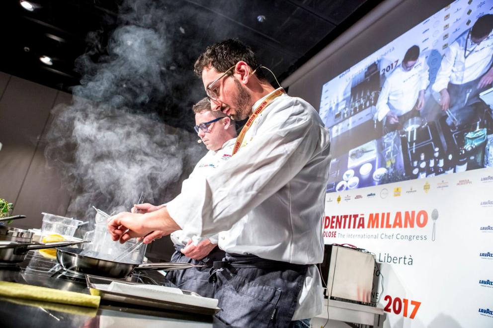 Galleria fotografica






ALFIO GHEZZI – Microclima: la distanza che accomuna - Fedele a se stesso e al titolo della sua lezione Alfio Ghezzi ha presentato la Tartiflette alla mia maniera, «una rivisitazione del frico, del rosti e della tartiflette; ma ho trovuto preparazioni simili anche in Norvegia», spiega. Per la sua tartiflette utilizza crema di patate, mortandela e un formaggio di pasta ottenuto dalla fermentazione di polvere di pasta precedentemente cotta in acqua per 50’ a 96° e poi essiccata in forno per un’intera notte









L’ingrediente principale del secondo piatto è lo yak della Val d’Ambiez, discendente dai buoi tibetani portati in Italia da Reinhold Messner, di cui Ghezzi ha impiattato la carne affiancandola a un crostino di pane di segale con lardo dello stesso yak, polvere di trombette nere, paprika affumicata, e - servito in tazza - a un brodo di carne di yak caramellata con miele e erbe









RICCARDO GASPARI con OLIVER PIRAS e ALESSANDRA DEL FAVERO Il “trip” del latte -Nell’agriturismo El Brite de Larieto l’alta cucina di Gaspari si sposa con le materie prime dell’allevamento di famiglia









Il salame di piedino di maiale con la sorpresa di un cubetto di lingua al suo interno cui fanno da cornice una gustosa di crema di siero di latte e nocciole tostate, sovrastato da una granita di mela (che dà una nota unica al piatto) e fiori di rosmarino è la summa dell’enunciato che nessuna materia è povera quando la si lavora a dovere. Il piedino di maiale è cotto nel latte, disossato e lavorato come un salame, da conservare al freddo «perché tende a spezzarsi». Il tocco finale è dato dal crumble di porcini e dalla rapa marinata









Bastano venti minuti per spostarsi da El Brite all’Aga di Oliver Piras e Alessandra Del Favero, ma l’ispirazione della cucina di Piras (sardo adottato dal Cadore in cui è stato spinto dall’amore) e Del Favero, coppia in cucina e nella vita, è diversa. Si capisce subito dal tiramisù, che di fatto non lo è pur ricordandone i sapori, ispirato da un loro viaggio in Giappone e dalla scoperta del koji, fungo utilizzato per la fermentazione della soja e del riso per fare miso e sake. Il dolce di Oliver e Alessandra ha una base di polenta di orzo di Belluno (presìdio Slow Food) fermentato e bruciato, è aromatizzato con infusione di radici di cicoria e completato da gelato di koji fatto con latte di El Brite









MAURIZIO GRANGE E PIERGIORGIO PELLEREI - I piatti della nostra tradizione visti con gli occhi della contemporaneità - Si può viaggiare anche rivisitando la tradizione. È un viaggio nel tempo quello di Maurizio Grange e Piergiorgio Pellerei fanno fare al piedino di maiale









Rosolato intero con sedano, carote e cipolle e poi cotto in un fondo di vitello per 2/3 ore prima di venire disossato, il piedino diventa con i carciofi il ripieno per il raviolone saltato al burro alle erbe. La presentazione è su una salsa di cavolfiori e zenzero deliziosamente piccante







