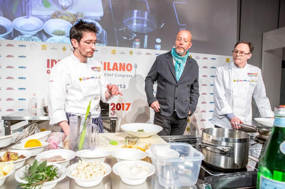 Galleria fotografica






ALFIO GHEZZI – Microclima: la distanza che accomuna - Fedele a se stesso e al titolo della sua lezione Alfio Ghezzi ha presentato la Tartiflette alla mia maniera, «una rivisitazione del frico, del rosti e della tartiflette; ma ho trovuto preparazioni simili anche in Norvegia», spiega. Per la sua tartiflette utilizza crema di patate, mortandela e un formaggio di pasta ottenuto dalla fermentazione di polvere di pasta precedentemente cotta in acqua per 50’ a 96° e poi essiccata in forno per un’intera notte









L’ingrediente principale del secondo piatto è lo yak della Val d’Ambiez, discendente dai buoi tibetani portati in Italia da Reinhold Messner, di cui Ghezzi ha impiattato la carne affiancandola a un crostino di pane di segale con lardo dello stesso yak, polvere di trombette nere, paprika affumicata, e - servito in tazza - a un brodo di carne di yak caramellata con miele e erbe









RICCARDO GASPARI con OLIVER PIRAS e ALESSANDRA DEL FAVERO Il “trip” del latte -Nell’agriturismo El Brite de Larieto l’alta cucina di Gaspari si sposa con le materie prime dell’allevamento di famiglia









Il salame di piedino di maiale con la sorpresa di un cubetto di lingua al suo interno cui fanno da cornice una gustosa di crema di siero di latte e nocciole tostate, sovrastato da una granita di mela (che dà una nota unica al piatto) e fiori di rosmarino è la summa dell’enunciato che nessuna materia è povera quando la si lavora a dovere. Il piedino di maiale è cotto nel latte, disossato e lavorato come un salame, da conservare al freddo «perché tende a spezzarsi». Il tocco finale è dato dal crumble di porcini e dalla rapa marinata









Bastano venti minuti per spostarsi da El Brite all’Aga di Oliver Piras e Alessandra Del Favero, ma l’ispirazione della cucina di Piras (sardo adottato dal Cadore in cui è stato spinto dall’amore) e Del Favero, coppia in cucina e nella vita, è diversa. Si capisce subito dal tiramisù, che di fatto non lo è pur ricordandone i sapori, ispirato da un loro viaggio in Giappone e dalla scoperta del koji, fungo utilizzato per la fermentazione della soja e del riso per fare miso e sake. Il dolce di Oliver e Alessandra ha una base di polenta di orzo di Belluno (presìdio Slow Food) fermentato e bruciato, è aromatizzato con infusione di radici di cicoria e completato da gelato di koji fatto con latte di El Brite






