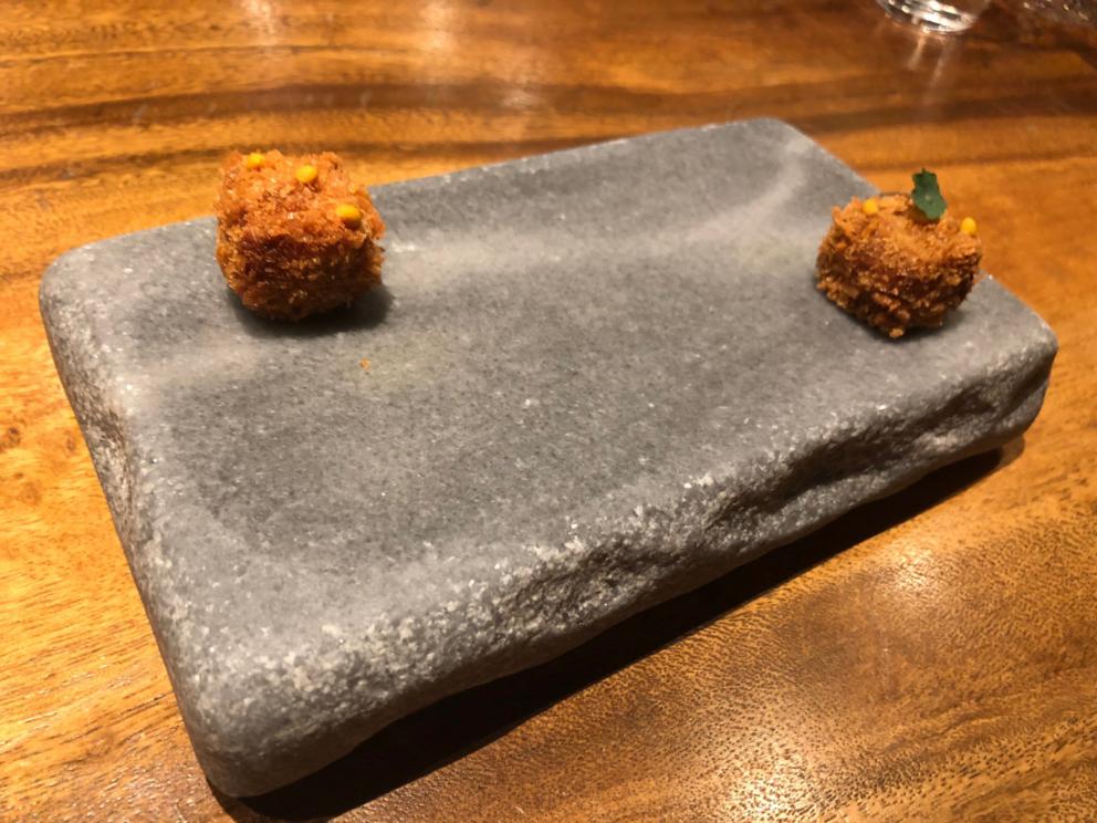 Photogallery






The sign appearing on Soi Langsuan in Bangkok, the little road where you can find restaurant Gaggan and, in front of it, the new-born Gaa, same ownership









The entrance to the restaurant, which recently got the second Michelin star. It’s open only in the evening. There are 65 people here who serve 100 clients daily, divided into two shifts (photo from themalaymailonline.com)









Gaggan’s famous emoji menu: "We first create the dish, then we sum it up with an emoji", he points out (photo from Andershusa/Instagram)









1 
Pink elderflower and watermelon
The tasting menu starts with the notes of the Foo Fighters. The entire first part of the menu is to be eaten with your hands: "This is how it works in India", he explains. First dish: a pearl among elderberry flowers and watermelon in an edible oyster shell. A debut to rinse the palate









2
Yogurt Explosion
Gaggan’s most famous dish. It’s the result of his early internship at elBulli in Roses, Catalonia. "If Ferran Adrià has had Spanish people accept a spherified olives", he says, "why shouldn’t I do the same with an emblem of India?". The spherified yogurt is made with low fat yogurt dipped in a sodium alginate









3
Lick it up. Mushroom peas
With "Lick it up", a hit from the Eighties by Kiss playing in the background, they serve this dish which you must hold with both hands and lick. The sauces, from bottom to top, in "licking order ": tomato, dehydrated mushrooms and mashed green chickpeas. On top, shaved truffle.  "Music, words, food. This is how we represent lightness"









Gaggan holds a cone









4
Tom Yum Kung
This is his version of Tom Yam (or Yum), a popular Thai soup. It’s a cold purée of tom yam served in crispy rice paper with a head of scampi to add flavour. It’s a sort of prawn cocktail in the shape of a cone









5
Goat brain, flower power
A cracker of goat brain ("to us Indians, it’s like foie gras", beams Gaggan) and rice flour. It is served to women first, playing with the similar sounds of flour and flower









6
Eggplant cookie
A cookie of aubergine, a sandwich the size of a coin, held together thanks to some onion chutney. "Out of 20, in Asia ingredients are usually worth 5, technique 15. With this dish I wanted to go in the opposite direction, return to Western minimalism with a universal emblem, that is to say aubergines. It’s a recent dish, which portraits the restaurant as it is now"









7
Chilly bon bon
Chilli pepper spheres. "Chocolates" filled with cumin, chilli pepper, ginger, and other spices. "In India there are four degrees of spiciness: hot, hotter, very hot and hell". The bon bon was mildly hot









8
Idly Sambar
Idly Sambar is a Tamil recipe, from the south of India: vegetable stew, tamarind and varying spices. "The world can be divided into two: those who eat rice, and those who eat bread. In this case, the base is bread made of fermented rice"









9
Banana chicken liver
"My daughter is one year and a half old. She’s difficult when it comes to eating. Give this combination to your children and they’ll be happy"









10
Fish Granola
Granola with fried seabass, walnuts and cheese cream









11
Gin tonic cucumber uni
Sea urchin cones, temaki, key lime and Indian tonic water. "This dish is the result of my trips to Japan: I went there 74 times only in the last couple of years. It has sea urchins from Hokkaido, in the north. In India we never eat raw food". The nori seaweed is made with dill









The selection of sea urchins from Hokkaido. "It’s worth its weight in gold", sighs Gaggan









12
Chutoro sushi
This is Gaggan’s homage to Tuna nigiri, an emblem of his future homeland (in 2021 after closing in Bangkok he’ll open a completely different restaurant in Fukuoka, Japan). Chutoro is a medium-fat tuna. In this case it is caramelised, adding a little emulsion of yuzu on top. The interesting part is below: it’s not rice, but a meringue made of all the ingredients used in sushi, that is to say vinegar, rice, sugar. "Sushi is a one way trip. You’ll never return. Nobody told me how to make it. This dish is a new take on a very personal memory"









13
Foie gras yuzu carrot
Carrot tartelette filled with foie gras. There’s no sweat on the hand: before the tasting they spray yuzu on the palm









Recipe number 14, another excursus between Japan and India









The dish is finished at the table









Whisking the mixture









14
Green vegetable matcha
Green apple gazpacho, cucumber and matcha tea. "I first fell in love with Japan thanks to tea. This looks like Japan but tastes of India and represents Gaggan"






