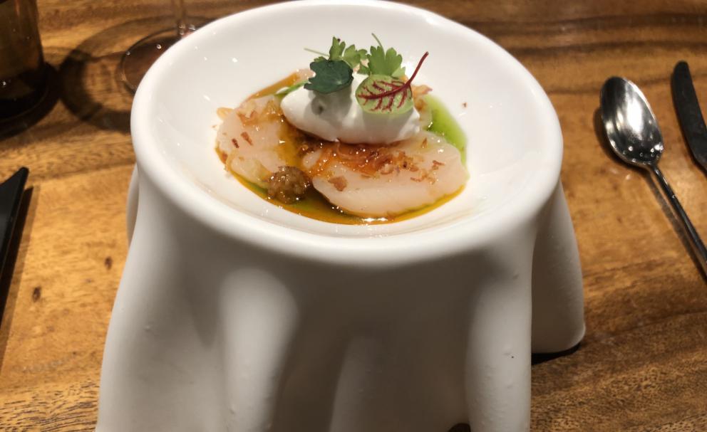 Photogallery






The sign appearing on Soi Langsuan in Bangkok, the little road where you can find restaurant Gaggan and, in front of it, the new-born Gaa, same ownership









The entrance to the restaurant, which recently got the second Michelin star. It’s open only in the evening. There are 65 people here who serve 100 clients daily, divided into two shifts (photo from themalaymailonline.com)









Gaggan’s famous emoji menu: "We first create the dish, then we sum it up with an emoji", he points out (photo from Andershusa/Instagram)









1 
Pink elderflower and watermelon
The tasting menu starts with the notes of the Foo Fighters. The entire first part of the menu is to be eaten with your hands: "This is how it works in India", he explains. First dish: a pearl among elderberry flowers and watermelon in an edible oyster shell. A debut to rinse the palate









2
Yogurt Explosion
Gaggan’s most famous dish. It’s the result of his early internship at elBulli in Roses, Catalonia. "If Ferran Adrià has had Spanish people accept a spherified olives", he says, "why shouldn’t I do the same with an emblem of India?". The spherified yogurt is made with low fat yogurt dipped in a sodium alginate









3
Lick it up. Mushroom peas
With "Lick it up", a hit from the Eighties by Kiss playing in the background, they serve this dish which you must hold with both hands and lick. The sauces, from bottom to top, in "licking order ": tomato, dehydrated mushrooms and mashed green chickpeas. On top, shaved truffle.  "Music, words, food. This is how we represent lightness"









Gaggan holds a cone









4
Tom Yum Kung
This is his version of Tom Yam (or Yum), a popular Thai soup. It’s a cold purée of tom yam served in crispy rice paper with a head of scampi to add flavour. It’s a sort of prawn cocktail in the shape of a cone









5
Goat brain, flower power
A cracker of goat brain ("to us Indians, it’s like foie gras", beams Gaggan) and rice flour. It is served to women first, playing with the similar sounds of flour and flower









6
Eggplant cookie
A cookie of aubergine, a sandwich the size of a coin, held together thanks to some onion chutney. "Out of 20, in Asia ingredients are usually worth 5, technique 15. With this dish I wanted to go in the opposite direction, return to Western minimalism with a universal emblem, that is to say aubergines. It’s a recent dish, which portraits the restaurant as it is now"









7
Chilly bon bon
Chilli pepper spheres. "Chocolates" filled with cumin, chilli pepper, ginger, and other spices. "In India there are four degrees of spiciness: hot, hotter, very hot and hell". The bon bon was mildly hot









8
Idly Sambar
Idly Sambar is a Tamil recipe, from the south of India: vegetable stew, tamarind and varying spices. "The world can be divided into two: those who eat rice, and those who eat bread. In this case, the base is bread made of fermented rice"









9
Banana chicken liver
"My daughter is one year and a half old. She’s difficult when it comes to eating. Give this combination to your children and they’ll be happy"









10
Fish Granola
Granola with fried seabass, walnuts and cheese cream









11
Gin tonic cucumber uni
Sea urchin cones, temaki, key lime and Indian tonic water. "This dish is the result of my trips to Japan: I went there 74 times only in the last couple of years. It has sea urchins from Hokkaido, in the north. In India we never eat raw food". The nori seaweed is made with dill









The selection of sea urchins from Hokkaido. "It’s worth its weight in gold", sighs Gaggan









12
Chutoro sushi
This is Gaggan’s homage to Tuna nigiri, an emblem of his future homeland (in 2021 after closing in Bangkok he’ll open a completely different restaurant in Fukuoka, Japan). Chutoro is a medium-fat tuna. In this case it is caramelised, adding a little emulsion of yuzu on top. The interesting part is below: it’s not rice, but a meringue made of all the ingredients used in sushi, that is to say vinegar, rice, sugar. "Sushi is a one way trip. You’ll never return. Nobody told me how to make it. This dish is a new take on a very personal memory"









13
Foie gras yuzu carrot
Carrot tartelette filled with foie gras. There’s no sweat on the hand: before the tasting they spray yuzu on the palm









Recipe number 14, another excursus between Japan and India









The dish is finished at the table









Whisking the mixture









14
Green vegetable matcha
Green apple gazpacho, cucumber and matcha tea. "I first fell in love with Japan thanks to tea. This looks like Japan but tastes of India and represents Gaggan"









15
Pork Vindaloo 
Vindaloo is a recipe from Goa, the Portuguese feud in west India. It’s pork, seasoned with garlic, vinegar and hot chilli pepper. In this case the fried texture is super-crispy, enriched with Japanese mustard which gives value to the Iberian pig marinated in wine and spices









New dishing out at the Chef's Table






