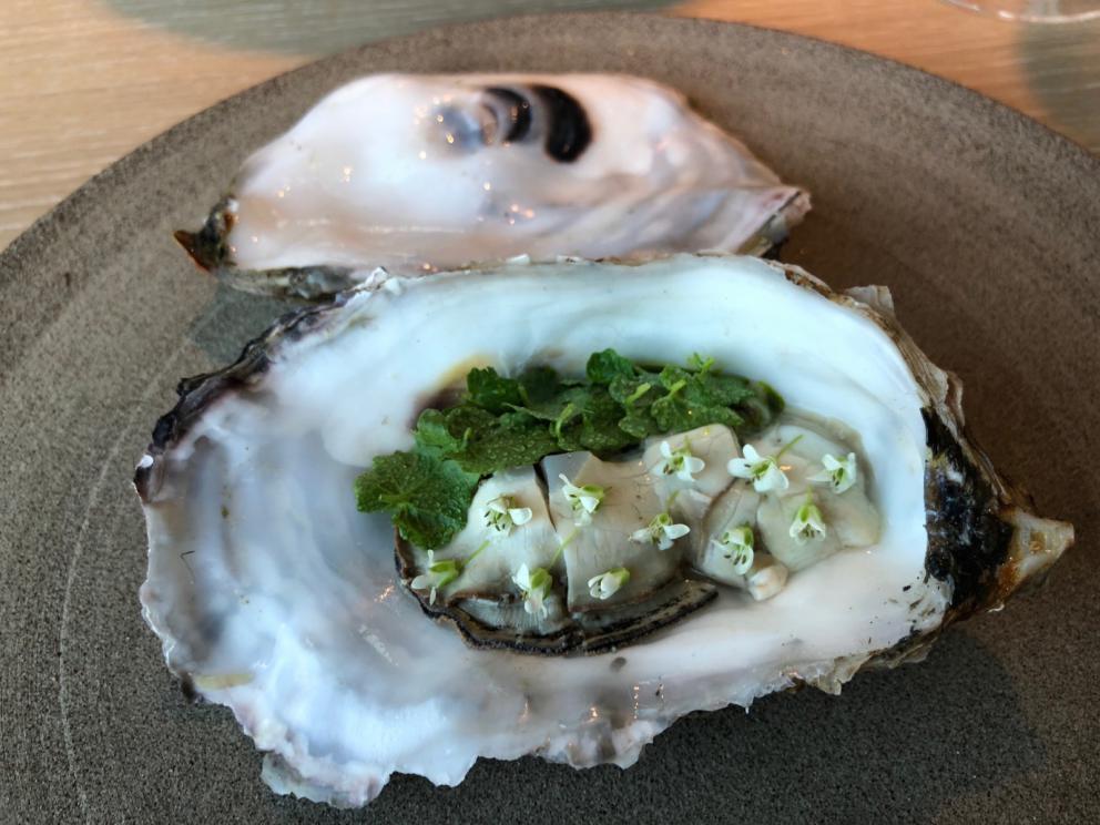 Photogallery






Noma 2.0 is in Christianshavn, the same neighbourhood as the first Noma. They’re 1.5 km apart, a 15 minutes’ walk. This picture shows the distance: to the right, there’s the warehouse of the old location (in Strandgade 93), to the left the smokestacks of Amager Bakke, the futuristic incinerator below which stands the new Noma (in Refshalevej 96)









Weather permitting, you can have a peaceful walk between the previous Noma to today’s Noma 









The new Noma is on an isthmus surrounded by canals. In the future they also want to reclaim some small parts for hydroponic farming









Bucolic scene with incinerator









Bikes left outside Noma. It’s the favourite means of transport among employees and interns









The long path taking you to the restaurant. The fence on the left shows how works are still in progress









On the two sides of the path there are the two new sections of the "Noma village", each with its specialty: grill, hot dishes, snacks, fermentations... In one month’s time, behind the fence we’ll have greenhouses, the test kitchen and the bread making area









To the left, before arriving at the restaurant, the future test kitchen. This will be run by Danish Mette Søberg with Riccardo Canella. "My first challenge?", reveals the latter, for a long time sous chef here, "is to work on the extraction of essential oils" 









The future Test Kitchen









The temporary gangway to the restaurant









Looking from the door to the restaurant, there’s a lake and the smokestacks puffing vapour from the Amager Bakke incinerator. It’s a futuristic project, both in terms of sustainability and architecture. It’s also known as Amager Slope or Copenhill, and its author is starchitect Bjarke Ingels, the same who designed the new Noma. Gradually opened in 2017, it transforms waste into electricity. The goal is to donate electricity to 62500 houses and hot water to 160000. It’s part of an ambitious project to transform Copenhagen into the first city in the world in terms of zero carbon dioxide emissions by 2025. By autumn this year, Amager Slope should open its ski slope, a climbing wall and a hiking track. You’ll be able to slalom on top of the incinerator









The windows from the dining room









Work is still in progress (photo taken on Thursday 22nd February 2018)









Traces of the old building, with barbwire. During WWII, they built bombs here









A view of the dining room at night (photo from Instagram/James Spreadbury)









The entrance to the restaurant









The usual ritual: a welcome from the entire staff, led by Rene Redzepi 









Behind the entrance, there are formaldehyde tanks with creatures from the abyss, shaped as in Damien Hirst’s works. The first image once you’re inside is to reproduce a Scandinavian village









The service kitchen is larger, more spacious and a completely open view from the dining room: "It’s the heart of our Scandinavian village", says Canella. There are 30 cooks working here now. 10 more, compared to the previous Noma









Large skylights above the cooks









There are currently more than 100 people working at Noma, of whom 63 are cooks - 26 employed, and 37 as interns









There’s fire in the kitchen, for the first time









On average, the dining room can host 40 people. "However", complains Redzepi, "there’s always someone who turns up with more people than the ones booked"









While the dining room is set, the outside space still need to be defined









The staff made the dining room decorations. There are no overly expensive designer objects









Dried fish









Seaweeds hanging from the ceiling









Dried octopus heads preserved in salt (with a balloon inside)














Bjarke Ingels and Redzepi’s plan included the wish to recreate a Danish farm









The luminous private dining room









The counter in the dining room. They drew the beams from the canals around the restaurant














The mise en place, bare and strictly without tablecloths









Water jug, candle, flower vase









A warm cloth, to begin with









Australian James Spreadbury, restaurant manager and partner at Noma









Welcome drink: Champagne extra brut Blanc d'Argile from Domaine Vouette et Sorbée









Sea Snail broth. The welcome dish at Noma is, as usual, a hot “soup”









Stefano Ferrano, from Torino, presents the following dish. There’s always a large Italian colony at Noma









Venus clams. Molluscs from Limfjord (Denmark) mixed with decorative clams, typical of Noma. Beside them, shells with blackcurrant oil and “Danish curry”, made with toasted coriander seeds, fennel and fennel seeds









The lid above the following dish. The mussels are not edible









Best of the mussel. Mussels open in a pan with water of fermented barley. «We recreate the mussel», says Canella, «using just the flaps, the best part». The paste is made with scraps from the mussel, cooked in smoked butter









The next dish is conceived and served by Riccardo Canella, the Paduan sous chef who conquered Redzepi, here with dining room intern Feline Hansen









Dried fruits and shrimps. In this case, the heads are not a decoration, but you must suck them –best not eat them because of the bones: they’re filled with a lovely prawn cream. The small crustaceans are still alive when they arrive on a ship straight from the Norwegian fjords









Inside, under the prawn broth skin, there’s fruits and vegetable preserved from the previous summer with raw prawns and gooseberry sauce with blackcurrant oil









How about beverages? There are three options, as usual: wine pairing (6 glasses plus a beer plus sake, 150 euros), juice pairing (juices and extracts, 110 euros) or a choice from the list. They recommend Champagne Chut... Libre from Val'Frison pour Dominique Derain, 50% Pinot Noir, 50% Chardonnay created by a couple who met at the old Noma. Well bodied, it will be a good match throughout the meal









As usual, the wine list starts with Champagne: the cheapest is 1400 crowns (190 euros)









White wines begin with labels from cold climates: first Austria, increasingly popular for its natural wines, then Germany, then all the others









How about Italy? Few names, among the white wines, from North and South









A dozen red/orange wines









Sea star, that is to say Cured trout roe and eggs, the emblem dish of this new era. They recommend moving the teaspoon from the heart to the edges of the tentacles. Aesthetics win over taste









Jellyfish. The jellyfish gel in the middle is in fact a clarified broth of calamari and recalls the texture of jellyfish. "We tried to cook jellyfish in 300 different ways but none was convincing so far". All around, pickled seaweed. The gel is almost tasteless, it serves to clean the palate after the pickles









Rene Redzepi himself presents the content of the first Seafood platter.









French style service with a small plate below for the empty shells









It’s made of two (per two) pieces: queen clam and mahogany clam









The Queen Clam is a very small variety of Norwegian scallop, seasoned with a vegetal reduction made with cucumber and peas miso. The red tip is the coral. "You should eat it using the top shell ", recommends Redzepi









The Mahogany clam is a centennial clam from the North Sea, very popular in Denmark and Iceland. «You can tell the age by the number of rings, like with trees», says Redzepi, «In 2007 they found one that was 450 years old. We’ve had it in the menu for a decade or so». The razor clam shell serves as teaspoon









Inside, there’s obviously not just a bare Mahogany. «We open it when the client arrives», says Canella, «remove the entrails and then slice it so as to preserve its firm texture». It’s seasoned with stir-fried gooseberry, capers of blackcurrants and blackcurrant sprouts preserved in vinegar. The sauce is made with mussel water









A note on the chairs: they’re more minimalistic. They’re no longer covered in sheepskin or leather from other Danish animals, in the style of Noma 1.0. The most significant element is the napkin: if you go to the toilet, they no longer replace it with a new one. There’s the old one, tied to the chair. "This is sustainability", they explain









The second seafood platter. It’s made of Sea cucumber and sour cream in various textures, including «chicharrones» (at 9 o’clock), sea urchins (at 12 and 3) and gigas oyster (at 6)









Sea urchins pressed in fresh cream and pumpkin seeds






