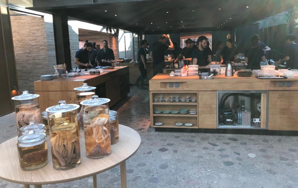 Photogallery






Noma 2.0 is in Christianshavn, the same neighbourhood as the first Noma. They’re 1.5 km apart, a 15 minutes’ walk. This picture shows the distance: to the right, there’s the warehouse of the old location (in Strandgade 93), to the left the smokestacks of Amager Bakke, the futuristic incinerator below which stands the new Noma (in Refshalevej 96)









Weather permitting, you can have a peaceful walk between the previous Noma to today’s Noma 









The new Noma is on an isthmus surrounded by canals. In the future they also want to reclaim some small parts for hydroponic farming









Bucolic scene with incinerator









Bikes left outside Noma. It’s the favourite means of transport among employees and interns









The long path taking you to the restaurant. The fence on the left shows how works are still in progress









On the two sides of the path there are the two new sections of the "Noma village", each with its specialty: grill, hot dishes, snacks, fermentations... In one month’s time, behind the fence we’ll have greenhouses, the test kitchen and the bread making area









To the left, before arriving at the restaurant, the future test kitchen. This will be run by Danish Mette Søberg with Riccardo Canella. "My first challenge?", reveals the latter, for a long time sous chef here, "is to work on the extraction of essential oils" 









The future Test Kitchen









The temporary gangway to the restaurant









Looking from the door to the restaurant, there’s a lake and the smokestacks puffing vapour from the Amager Bakke incinerator. It’s a futuristic project, both in terms of sustainability and architecture. It’s also known as Amager Slope or Copenhill, and its author is starchitect Bjarke Ingels, the same who designed the new Noma. Gradually opened in 2017, it transforms waste into electricity. The goal is to donate electricity to 62500 houses and hot water to 160000. It’s part of an ambitious project to transform Copenhagen into the first city in the world in terms of zero carbon dioxide emissions by 2025. By autumn this year, Amager Slope should open its ski slope, a climbing wall and a hiking track. You’ll be able to slalom on top of the incinerator









The windows from the dining room









Work is still in progress (photo taken on Thursday 22nd February 2018)









Traces of the old building, with barbwire. During WWII, they built bombs here









A view of the dining room at night (photo from Instagram/James Spreadbury)









The entrance to the restaurant









The usual ritual: a welcome from the entire staff, led by Rene Redzepi 









Behind the entrance, there are formaldehyde tanks with creatures from the abyss, shaped as in Damien Hirst’s works. The first image once you’re inside is to reproduce a Scandinavian village






