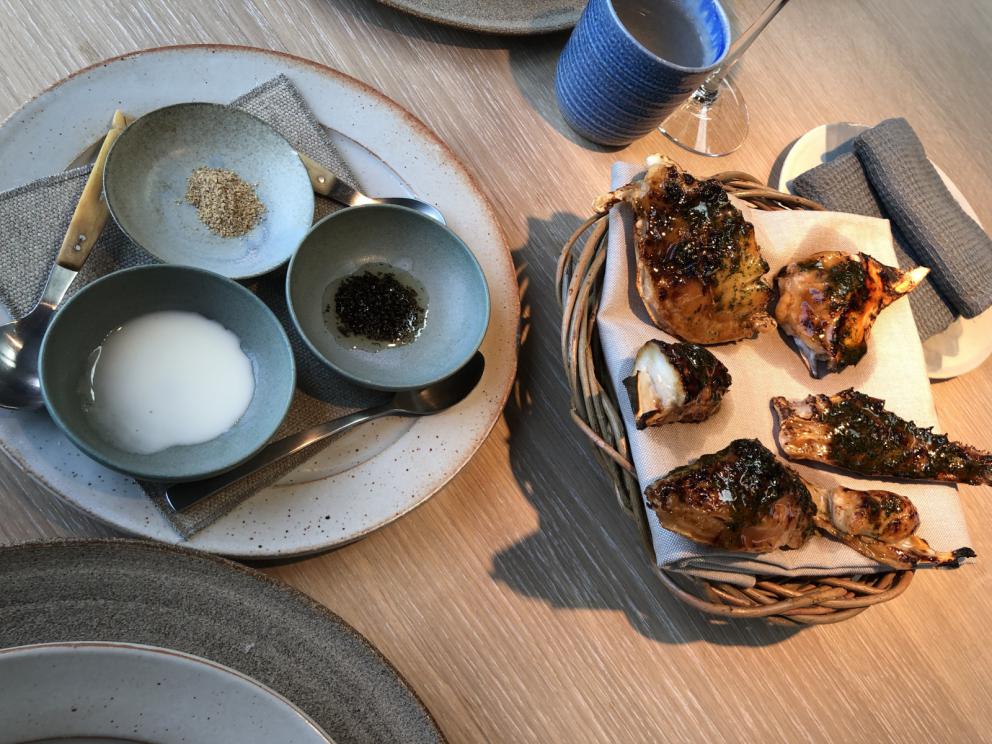 Photogallery






Noma 2.0 is in Christianshavn, the same neighbourhood as the first Noma. They’re 1.5 km apart, a 15 minutes’ walk. This picture shows the distance: to the right, there’s the warehouse of the old location (in Strandgade 93), to the left the smokestacks of Amager Bakke, the futuristic incinerator below which stands the new Noma (in Refshalevej 96)









Weather permitting, you can have a peaceful walk between the previous Noma to today’s Noma 









The new Noma is on an isthmus surrounded by canals. In the future they also want to reclaim some small parts for hydroponic farming









Bucolic scene with incinerator









Bikes left outside Noma. It’s the favourite means of transport among employees and interns









The long path taking you to the restaurant. The fence on the left shows how works are still in progress









On the two sides of the path there are the two new sections of the "Noma village", each with its specialty: grill, hot dishes, snacks, fermentations... In one month’s time, behind the fence we’ll have greenhouses, the test kitchen and the bread making area









To the left, before arriving at the restaurant, the future test kitchen. This will be run by Danish Mette Søberg with Riccardo Canella. "My first challenge?", reveals the latter, for a long time sous chef here, "is to work on the extraction of essential oils" 









The future Test Kitchen









The temporary gangway to the restaurant









Looking from the door to the restaurant, there’s a lake and the smokestacks puffing vapour from the Amager Bakke incinerator. It’s a futuristic project, both in terms of sustainability and architecture. It’s also known as Amager Slope or Copenhill, and its author is starchitect Bjarke Ingels, the same who designed the new Noma. Gradually opened in 2017, it transforms waste into electricity. The goal is to donate electricity to 62500 houses and hot water to 160000. It’s part of an ambitious project to transform Copenhagen into the first city in the world in terms of zero carbon dioxide emissions by 2025. By autumn this year, Amager Slope should open its ski slope, a climbing wall and a hiking track. You’ll be able to slalom on top of the incinerator









The windows from the dining room









Work is still in progress (photo taken on Thursday 22nd February 2018)









Traces of the old building, with barbwire. During WWII, they built bombs here









A view of the dining room at night (photo from Instagram/James Spreadbury)









The entrance to the restaurant









The usual ritual: a welcome from the entire staff, led by Rene Redzepi 









Behind the entrance, there are formaldehyde tanks with creatures from the abyss, shaped as in Damien Hirst’s works. The first image once you’re inside is to reproduce a Scandinavian village









The service kitchen is larger, more spacious and a completely open view from the dining room: "It’s the heart of our Scandinavian village", says Canella. There are 30 cooks working here now. 10 more, compared to the previous Noma









Large skylights above the cooks









There are currently more than 100 people working at Noma, of whom 63 are cooks - 26 employed, and 37 as interns









There’s fire in the kitchen, for the first time









On average, the dining room can host 40 people. "However", complains Redzepi, "there’s always someone who turns up with more people than the ones booked"









While the dining room is set, the outside space still need to be defined









The staff made the dining room decorations. There are no overly expensive designer objects









Dried fish









Seaweeds hanging from the ceiling









Dried octopus heads preserved in salt (with a balloon inside)














Bjarke Ingels and Redzepi’s plan included the wish to recreate a Danish farm









The luminous private dining room









The counter in the dining room. They drew the beams from the canals around the restaurant














The mise en place, bare and strictly without tablecloths









Water jug, candle, flower vase









A warm cloth, to begin with









Australian James Spreadbury, restaurant manager and partner at Noma









Welcome drink: Champagne extra brut Blanc d'Argile from Domaine Vouette et Sorbée









Sea Snail broth. The welcome dish at Noma is, as usual, a hot “soup”









Stefano Ferrano, from Torino, presents the following dish. There’s always a large Italian colony at Noma









Venus clams. Molluscs from Limfjord (Denmark) mixed with decorative clams, typical of Noma. Beside them, shells with blackcurrant oil and “Danish curry”, made with toasted coriander seeds, fennel and fennel seeds









The lid above the following dish. The mussels are not edible









Best of the mussel. Mussels open in a pan with water of fermented barley. «We recreate the mussel», says Canella, «using just the flaps, the best part». The paste is made with scraps from the mussel, cooked in smoked butter









The next dish is conceived and served by Riccardo Canella, the Paduan sous chef who conquered Redzepi, here with dining room intern Feline Hansen









Dried fruits and shrimps. In this case, the heads are not a decoration, but you must suck them –best not eat them because of the bones: they’re filled with a lovely prawn cream. The small crustaceans are still alive when they arrive on a ship straight from the Norwegian fjords









Inside, under the prawn broth skin, there’s fruits and vegetable preserved from the previous summer with raw prawns and gooseberry sauce with blackcurrant oil









How about beverages? There are three options, as usual: wine pairing (6 glasses plus a beer plus sake, 150 euros), juice pairing (juices and extracts, 110 euros) or a choice from the list. They recommend Champagne Chut... Libre from Val'Frison pour Dominique Derain, 50% Pinot Noir, 50% Chardonnay created by a couple who met at the old Noma. Well bodied, it will be a good match throughout the meal









As usual, the wine list starts with Champagne: the cheapest is 1400 crowns (190 euros)









White wines begin with labels from cold climates: first Austria, increasingly popular for its natural wines, then Germany, then all the others









How about Italy? Few names, among the white wines, from North and South









A dozen red/orange wines









Sea star, that is to say Cured trout roe and eggs, the emblem dish of this new era. They recommend moving the teaspoon from the heart to the edges of the tentacles. Aesthetics win over taste









Jellyfish. The jellyfish gel in the middle is in fact a clarified broth of calamari and recalls the texture of jellyfish. "We tried to cook jellyfish in 300 different ways but none was convincing so far". All around, pickled seaweed. The gel is almost tasteless, it serves to clean the palate after the pickles









Rene Redzepi himself presents the content of the first Seafood platter.









French style service with a small plate below for the empty shells









It’s made of two (per two) pieces: queen clam and mahogany clam









The Queen Clam is a very small variety of Norwegian scallop, seasoned with a vegetal reduction made with cucumber and peas miso. The red tip is the coral. "You should eat it using the top shell ", recommends Redzepi









The Mahogany clam is a centennial clam from the North Sea, very popular in Denmark and Iceland. «You can tell the age by the number of rings, like with trees», says Redzepi, «In 2007 they found one that was 450 years old. We’ve had it in the menu for a decade or so». The razor clam shell serves as teaspoon









Inside, there’s obviously not just a bare Mahogany. «We open it when the client arrives», says Canella, «remove the entrails and then slice it so as to preserve its firm texture». It’s seasoned with stir-fried gooseberry, capers of blackcurrants and blackcurrant sprouts preserved in vinegar. The sauce is made with mussel water









A note on the chairs: they’re more minimalistic. They’re no longer covered in sheepskin or leather from other Danish animals, in the style of Noma 1.0. The most significant element is the napkin: if you go to the toilet, they no longer replace it with a new one. There’s the old one, tied to the chair. "This is sustainability", they explain









The second seafood platter. It’s made of Sea cucumber and sour cream in various textures, including «chicharrones» (at 9 o’clock), sea urchins (at 12 and 3) and gigas oyster (at 6)









Sea urchins pressed in fresh cream and pumpkin seeds









Giga Oyster, a huge oyster from the Pacific, quickly steamed and garnished with pickles. Noma only reserved one thousand of these. In the menu until available









The following dish, off the menu, is again from Canella: horse mussel ragout, rare specimen of which 30 arrive at 'Noma each week









They cook the mussel as if it were kidney, in a sort of Bolognese sauce but with ginger. Ginger? "Yes, we’ve decided to include it, as with other spices, after our Mexican experience"









Another Italian presents a dish, Edoardo Fiaschi from Prato, at Noma for 3 years now









Squid in seaweed butter. An almost neglected Danish squid lightly seared in fermented koji oil, rolled and seasoned with seaweed butter and served on sticks of blackcurrant that widen its aromas. Formidable and beautiful









The following dish is inside a nice bee wax container. It’s made with balloons covered multiple times in bee wax. «We spent weeks making them. We’ve made thousands». They’re disposable...









Sea snail and roses. They recommend to: "Eat it keeping the bee wax on your hands "









Sea snail. Another small nibble from the top part of the sea snail, lightly warmed up in water and served on a reduction of lemon thyme









A sea snail toothpick, initially carved by Redzepi himself






