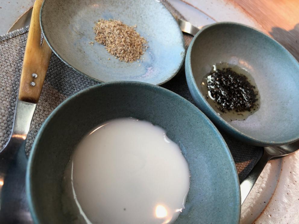 Photogallery






Noma 2.0 is in Christianshavn, the same neighbourhood as the first Noma. They’re 1.5 km apart, a 15 minutes’ walk. This picture shows the distance: to the right, there’s the warehouse of the old location (in Strandgade 93), to the left the smokestacks of Amager Bakke, the futuristic incinerator below which stands the new Noma (in Refshalevej 96)









Weather permitting, you can have a peaceful walk between the previous Noma to today’s Noma 









The new Noma is on an isthmus surrounded by canals. In the future they also want to reclaim some small parts for hydroponic farming









Bucolic scene with incinerator









Bikes left outside Noma. It’s the favourite means of transport among employees and interns









The long path taking you to the restaurant. The fence on the left shows how works are still in progress









On the two sides of the path there are the two new sections of the "Noma village", each with its specialty: grill, hot dishes, snacks, fermentations... In one month’s time, behind the fence we’ll have greenhouses, the test kitchen and the bread making area









To the left, before arriving at the restaurant, the future test kitchen. This will be run by Danish Mette Søberg with Riccardo Canella. "My first challenge?", reveals the latter, for a long time sous chef here, "is to work on the extraction of essential oils" 









The future Test Kitchen









The temporary gangway to the restaurant









Looking from the door to the restaurant, there’s a lake and the smokestacks puffing vapour from the Amager Bakke incinerator. It’s a futuristic project, both in terms of sustainability and architecture. It’s also known as Amager Slope or Copenhill, and its author is starchitect Bjarke Ingels, the same who designed the new Noma. Gradually opened in 2017, it transforms waste into electricity. The goal is to donate electricity to 62500 houses and hot water to 160000. It’s part of an ambitious project to transform Copenhagen into the first city in the world in terms of zero carbon dioxide emissions by 2025. By autumn this year, Amager Slope should open its ski slope, a climbing wall and a hiking track. You’ll be able to slalom on top of the incinerator









The windows from the dining room









Work is still in progress (photo taken on Thursday 22nd February 2018)









Traces of the old building, with barbwire. During WWII, they built bombs here









A view of the dining room at night (photo from Instagram/James Spreadbury)









The entrance to the restaurant









The usual ritual: a welcome from the entire staff, led by Rene Redzepi 









Behind the entrance, there are formaldehyde tanks with creatures from the abyss, shaped as in Damien Hirst’s works. The first image once you’re inside is to reproduce a Scandinavian village









The service kitchen is larger, more spacious and a completely open view from the dining room: "It’s the heart of our Scandinavian village", says Canella. There are 30 cooks working here now. 10 more, compared to the previous Noma









Large skylights above the cooks









There are currently more than 100 people working at Noma, of whom 63 are cooks - 26 employed, and 37 as interns









There’s fire in the kitchen, for the first time









On average, the dining room can host 40 people. "However", complains Redzepi, "there’s always someone who turns up with more people than the ones booked"









While the dining room is set, the outside space still need to be defined









The staff made the dining room decorations. There are no overly expensive designer objects









Dried fish









Seaweeds hanging from the ceiling









Dried octopus heads preserved in salt (with a balloon inside)














Bjarke Ingels and Redzepi’s plan included the wish to recreate a Danish farm









The luminous private dining room









The counter in the dining room. They drew the beams from the canals around the restaurant














The mise en place, bare and strictly without tablecloths









Water jug, candle, flower vase









A warm cloth, to begin with









Australian James Spreadbury, restaurant manager and partner at Noma









Welcome drink: Champagne extra brut Blanc d'Argile from Domaine Vouette et Sorbée









Sea Snail broth. The welcome dish at Noma is, as usual, a hot “soup”









Stefano Ferrano, from Torino, presents the following dish. There’s always a large Italian colony at Noma









Venus clams. Molluscs from Limfjord (Denmark) mixed with decorative clams, typical of Noma. Beside them, shells with blackcurrant oil and “Danish curry”, made with toasted coriander seeds, fennel and fennel seeds









The lid above the following dish. The mussels are not edible









Best of the mussel. Mussels open in a pan with water of fermented barley. «We recreate the mussel», says Canella, «using just the flaps, the best part». The paste is made with scraps from the mussel, cooked in smoked butter









The next dish is conceived and served by Riccardo Canella, the Paduan sous chef who conquered Redzepi, here with dining room intern Feline Hansen









Dried fruits and shrimps. In this case, the heads are not a decoration, but you must suck them –best not eat them because of the bones: they’re filled with a lovely prawn cream. The small crustaceans are still alive when they arrive on a ship straight from the Norwegian fjords









Inside, under the prawn broth skin, there’s fruits and vegetable preserved from the previous summer with raw prawns and gooseberry sauce with blackcurrant oil









How about beverages? There are three options, as usual: wine pairing (6 glasses plus a beer plus sake, 150 euros), juice pairing (juices and extracts, 110 euros) or a choice from the list. They recommend Champagne Chut... Libre from Val'Frison pour Dominique Derain, 50% Pinot Noir, 50% Chardonnay created by a couple who met at the old Noma. Well bodied, it will be a good match throughout the meal









As usual, the wine list starts with Champagne: the cheapest is 1400 crowns (190 euros)









White wines begin with labels from cold climates: first Austria, increasingly popular for its natural wines, then Germany, then all the others









How about Italy? Few names, among the white wines, from North and South









A dozen red/orange wines









Sea star, that is to say Cured trout roe and eggs, the emblem dish of this new era. They recommend moving the teaspoon from the heart to the edges of the tentacles. Aesthetics win over taste









Jellyfish. The jellyfish gel in the middle is in fact a clarified broth of calamari and recalls the texture of jellyfish. "We tried to cook jellyfish in 300 different ways but none was convincing so far". All around, pickled seaweed. The gel is almost tasteless, it serves to clean the palate after the pickles









Rene Redzepi himself presents the content of the first Seafood platter.









French style service with a small plate below for the empty shells









It’s made of two (per two) pieces: queen clam and mahogany clam









The Queen Clam is a very small variety of Norwegian scallop, seasoned with a vegetal reduction made with cucumber and peas miso. The red tip is the coral. "You should eat it using the top shell ", recommends Redzepi









The Mahogany clam is a centennial clam from the North Sea, very popular in Denmark and Iceland. «You can tell the age by the number of rings, like with trees», says Redzepi, «In 2007 they found one that was 450 years old. We’ve had it in the menu for a decade or so». The razor clam shell serves as teaspoon









Inside, there’s obviously not just a bare Mahogany. «We open it when the client arrives», says Canella, «remove the entrails and then slice it so as to preserve its firm texture». It’s seasoned with stir-fried gooseberry, capers of blackcurrants and blackcurrant sprouts preserved in vinegar. The sauce is made with mussel water









A note on the chairs: they’re more minimalistic. They’re no longer covered in sheepskin or leather from other Danish animals, in the style of Noma 1.0. The most significant element is the napkin: if you go to the toilet, they no longer replace it with a new one. There’s the old one, tied to the chair. "This is sustainability", they explain









The second seafood platter. It’s made of Sea cucumber and sour cream in various textures, including «chicharrones» (at 9 o’clock), sea urchins (at 12 and 3) and gigas oyster (at 6)









Sea urchins pressed in fresh cream and pumpkin seeds









Giga Oyster, a huge oyster from the Pacific, quickly steamed and garnished with pickles. Noma only reserved one thousand of these. In the menu until available









The following dish, off the menu, is again from Canella: horse mussel ragout, rare specimen of which 30 arrive at 'Noma each week









They cook the mussel as if it were kidney, in a sort of Bolognese sauce but with ginger. Ginger? "Yes, we’ve decided to include it, as with other spices, after our Mexican experience"









Another Italian presents a dish, Edoardo Fiaschi from Prato, at Noma for 3 years now









Squid in seaweed butter. An almost neglected Danish squid lightly seared in fermented koji oil, rolled and seasoned with seaweed butter and served on sticks of blackcurrant that widen its aromas. Formidable and beautiful









The following dish is inside a nice bee wax container. It’s made with balloons covered multiple times in bee wax. «We spent weeks making them. We’ve made thousands». They’re disposable...









Sea snail and roses. They recommend to: "Eat it keeping the bee wax on your hands "









Sea snail. Another small nibble from the top part of the sea snail, lightly warmed up in water and served on a reduction of lemon thyme









A sea snail toothpick, initially carved by Redzepi himself









Head of the cod, (right), the real main course at Noma









Another rather laborious recipe. «It takes half an hour just to separate the head. We remove the skin, the collagen, we cut mandibles, tongue, cheek and the part behind. We rinse it in water, spices, koji and cook it in the yakitori with a glaze of mushrooms and spiced fennel broth»






