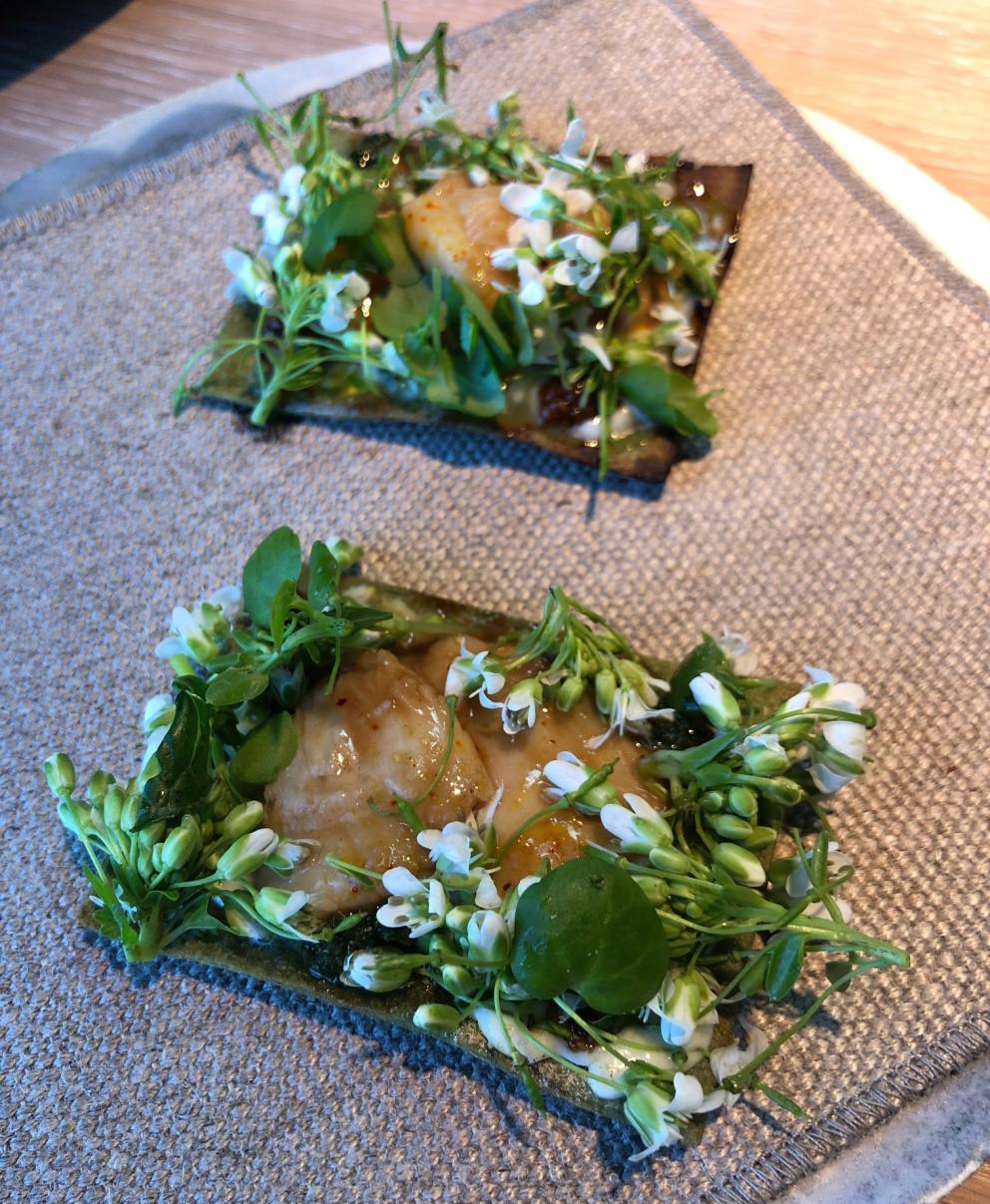 Photogallery






Noma 2.0 is in Christianshavn, the same neighbourhood as the first Noma. They’re 1.5 km apart, a 15 minutes’ walk. This picture shows the distance: to the right, there’s the warehouse of the old location (in Strandgade 93), to the left the smokestacks of Amager Bakke, the futuristic incinerator below which stands the new Noma (in Refshalevej 96)









Weather permitting, you can have a peaceful walk between the previous Noma to today’s Noma 









The new Noma is on an isthmus surrounded by canals. In the future they also want to reclaim some small parts for hydroponic farming









Bucolic scene with incinerator









Bikes left outside Noma. It’s the favourite means of transport among employees and interns









The long path taking you to the restaurant. The fence on the left shows how works are still in progress









On the two sides of the path there are the two new sections of the "Noma village", each with its specialty: grill, hot dishes, snacks, fermentations... In one month’s time, behind the fence we’ll have greenhouses, the test kitchen and the bread making area









To the left, before arriving at the restaurant, the future test kitchen. This will be run by Danish Mette Søberg with Riccardo Canella. "My first challenge?", reveals the latter, for a long time sous chef here, "is to work on the extraction of essential oils" 









The future Test Kitchen









The temporary gangway to the restaurant









Looking from the door to the restaurant, there’s a lake and the smokestacks puffing vapour from the Amager Bakke incinerator. It’s a futuristic project, both in terms of sustainability and architecture. It’s also known as Amager Slope or Copenhill, and its author is starchitect Bjarke Ingels, the same who designed the new Noma. Gradually opened in 2017, it transforms waste into electricity. The goal is to donate electricity to 62500 houses and hot water to 160000. It’s part of an ambitious project to transform Copenhagen into the first city in the world in terms of zero carbon dioxide emissions by 2025. By autumn this year, Amager Slope should open its ski slope, a climbing wall and a hiking track. You’ll be able to slalom on top of the incinerator









The windows from the dining room









Work is still in progress (photo taken on Thursday 22nd February 2018)









Traces of the old building, with barbwire. During WWII, they built bombs here









A view of the dining room at night (photo from Instagram/James Spreadbury)









The entrance to the restaurant









The usual ritual: a welcome from the entire staff, led by Rene Redzepi 









Behind the entrance, there are formaldehyde tanks with creatures from the abyss, shaped as in Damien Hirst’s works. The first image once you’re inside is to reproduce a Scandinavian village









The service kitchen is larger, more spacious and a completely open view from the dining room: "It’s the heart of our Scandinavian village", says Canella. There are 30 cooks working here now. 10 more, compared to the previous Noma









Large skylights above the cooks









There are currently more than 100 people working at Noma, of whom 63 are cooks - 26 employed, and 37 as interns









There’s fire in the kitchen, for the first time









On average, the dining room can host 40 people. "However", complains Redzepi, "there’s always someone who turns up with more people than the ones booked"









While the dining room is set, the outside space still need to be defined









The staff made the dining room decorations. There are no overly expensive designer objects









Dried fish









Seaweeds hanging from the ceiling









Dried octopus heads preserved in salt (with a balloon inside)














Bjarke Ingels and Redzepi’s plan included the wish to recreate a Danish farm









The luminous private dining room









The counter in the dining room. They drew the beams from the canals around the restaurant














The mise en place, bare and strictly without tablecloths









Water jug, candle, flower vase









A warm cloth, to begin with









Australian James Spreadbury, restaurant manager and partner at Noma









Welcome drink: Champagne extra brut Blanc d'Argile from Domaine Vouette et Sorbée









Sea Snail broth. The welcome dish at Noma is, as usual, a hot “soup”









Stefano Ferrano, from Torino, presents the following dish. There’s always a large Italian colony at Noma









Venus clams. Molluscs from Limfjord (Denmark) mixed with decorative clams, typical of Noma. Beside them, shells with blackcurrant oil and “Danish curry”, made with toasted coriander seeds, fennel and fennel seeds









The lid above the following dish. The mussels are not edible









Best of the mussel. Mussels open in a pan with water of fermented barley. «We recreate the mussel», says Canella, «using just the flaps, the best part». The paste is made with scraps from the mussel, cooked in smoked butter









The next dish is conceived and served by Riccardo Canella, the Paduan sous chef who conquered Redzepi, here with dining room intern Feline Hansen









Dried fruits and shrimps. In this case, the heads are not a decoration, but you must suck them –best not eat them because of the bones: they’re filled with a lovely prawn cream. The small crustaceans are still alive when they arrive on a ship straight from the Norwegian fjords









Inside, under the prawn broth skin, there’s fruits and vegetable preserved from the previous summer with raw prawns and gooseberry sauce with blackcurrant oil









How about beverages? There are three options, as usual: wine pairing (6 glasses plus a beer plus sake, 150 euros), juice pairing (juices and extracts, 110 euros) or a choice from the list. They recommend Champagne Chut... Libre from Val'Frison pour Dominique Derain, 50% Pinot Noir, 50% Chardonnay created by a couple who met at the old Noma. Well bodied, it will be a good match throughout the meal









As usual, the wine list starts with Champagne: the cheapest is 1400 crowns (190 euros)









White wines begin with labels from cold climates: first Austria, increasingly popular for its natural wines, then Germany, then all the others









How about Italy? Few names, among the white wines, from North and South









A dozen red/orange wines









Sea star, that is to say Cured trout roe and eggs, the emblem dish of this new era. They recommend moving the teaspoon from the heart to the edges of the tentacles. Aesthetics win over taste









Jellyfish. The jellyfish gel in the middle is in fact a clarified broth of calamari and recalls the texture of jellyfish. "We tried to cook jellyfish in 300 different ways but none was convincing so far". All around, pickled seaweed. The gel is almost tasteless, it serves to clean the palate after the pickles









Rene Redzepi himself presents the content of the first Seafood platter.









French style service with a small plate below for the empty shells









It’s made of two (per two) pieces: queen clam and mahogany clam









The Queen Clam is a very small variety of Norwegian scallop, seasoned with a vegetal reduction made with cucumber and peas miso. The red tip is the coral. "You should eat it using the top shell ", recommends Redzepi









The Mahogany clam is a centennial clam from the North Sea, very popular in Denmark and Iceland. «You can tell the age by the number of rings, like with trees», says Redzepi, «In 2007 they found one that was 450 years old. We’ve had it in the menu for a decade or so». The razor clam shell serves as teaspoon









Inside, there’s obviously not just a bare Mahogany. «We open it when the client arrives», says Canella, «remove the entrails and then slice it so as to preserve its firm texture». It’s seasoned with stir-fried gooseberry, capers of blackcurrants and blackcurrant sprouts preserved in vinegar. The sauce is made with mussel water









A note on the chairs: they’re more minimalistic. They’re no longer covered in sheepskin or leather from other Danish animals, in the style of Noma 1.0. The most significant element is the napkin: if you go to the toilet, they no longer replace it with a new one. There’s the old one, tied to the chair. "This is sustainability", they explain









The second seafood platter. It’s made of Sea cucumber and sour cream in various textures, including «chicharrones» (at 9 o’clock), sea urchins (at 12 and 3) and gigas oyster (at 6)









Sea urchins pressed in fresh cream and pumpkin seeds









Giga Oyster, a huge oyster from the Pacific, quickly steamed and garnished with pickles. Noma only reserved one thousand of these. In the menu until available









The following dish, off the menu, is again from Canella: horse mussel ragout, rare specimen of which 30 arrive at 'Noma each week









They cook the mussel as if it were kidney, in a sort of Bolognese sauce but with ginger. Ginger? "Yes, we’ve decided to include it, as with other spices, after our Mexican experience"









Another Italian presents a dish, Edoardo Fiaschi from Prato, at Noma for 3 years now









Squid in seaweed butter. An almost neglected Danish squid lightly seared in fermented koji oil, rolled and seasoned with seaweed butter and served on sticks of blackcurrant that widen its aromas. Formidable and beautiful









The following dish is inside a nice bee wax container. It’s made with balloons covered multiple times in bee wax. «We spent weeks making them. We’ve made thousands». They’re disposable...









Sea snail and roses. They recommend to: "Eat it keeping the bee wax on your hands "









Sea snail. Another small nibble from the top part of the sea snail, lightly warmed up in water and served on a reduction of lemon thyme









A sea snail toothpick, initially carved by Redzepi himself









Head of the cod, (right), the real main course at Noma









Another rather laborious recipe. «It takes half an hour just to separate the head. We remove the skin, the collagen, we cut mandibles, tongue, cheek and the part behind. We rinse it in water, spices, koji and cook it in the yakitori with a glaze of mushrooms and spiced fennel broth»









You can garnish the cod as you choose, with a paste of ants (top right corner), a slightly spicy emulsion of koji oil, water and horseradish sauce (left) and Danish curry (bottom)









On the side of the cod, there’s also wild garlic seasoned with smoked butter and roasted yeast. Intense flavour









Cod bones after the tasting






