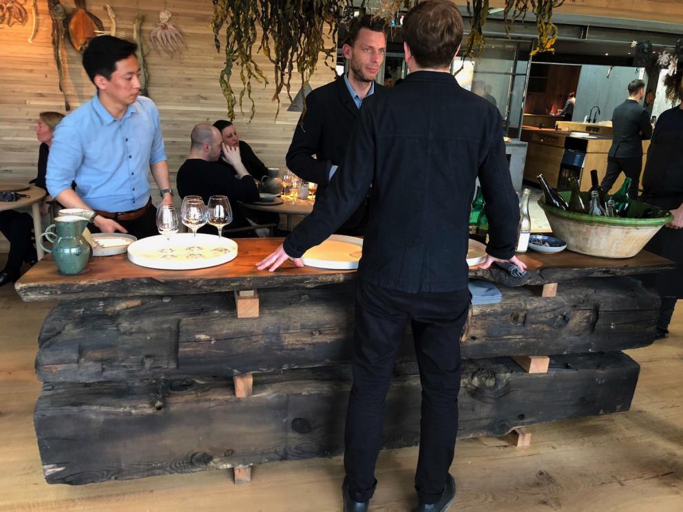 Photogallery






Noma 2.0 is in Christianshavn, the same neighbourhood as the first Noma. They’re 1.5 km apart, a 15 minutes’ walk. This picture shows the distance: to the right, there’s the warehouse of the old location (in Strandgade 93), to the left the smokestacks of Amager Bakke, the futuristic incinerator below which stands the new Noma (in Refshalevej 96)









Weather permitting, you can have a peaceful walk between the previous Noma to today’s Noma 









The new Noma is on an isthmus surrounded by canals. In the future they also want to reclaim some small parts for hydroponic farming









Bucolic scene with incinerator









Bikes left outside Noma. It’s the favourite means of transport among employees and interns









The long path taking you to the restaurant. The fence on the left shows how works are still in progress









On the two sides of the path there are the two new sections of the "Noma village", each with its specialty: grill, hot dishes, snacks, fermentations... In one month’s time, behind the fence we’ll have greenhouses, the test kitchen and the bread making area









To the left, before arriving at the restaurant, the future test kitchen. This will be run by Danish Mette Søberg with Riccardo Canella. "My first challenge?", reveals the latter, for a long time sous chef here, "is to work on the extraction of essential oils" 









The future Test Kitchen









The temporary gangway to the restaurant









Looking from the door to the restaurant, there’s a lake and the smokestacks puffing vapour from the Amager Bakke incinerator. It’s a futuristic project, both in terms of sustainability and architecture. It’s also known as Amager Slope or Copenhill, and its author is starchitect Bjarke Ingels, the same who designed the new Noma. Gradually opened in 2017, it transforms waste into electricity. The goal is to donate electricity to 62500 houses and hot water to 160000. It’s part of an ambitious project to transform Copenhagen into the first city in the world in terms of zero carbon dioxide emissions by 2025. By autumn this year, Amager Slope should open its ski slope, a climbing wall and a hiking track. You’ll be able to slalom on top of the incinerator









The windows from the dining room









Work is still in progress (photo taken on Thursday 22nd February 2018)









Traces of the old building, with barbwire. During WWII, they built bombs here









A view of the dining room at night (photo from Instagram/James Spreadbury)









The entrance to the restaurant









The usual ritual: a welcome from the entire staff, led by Rene Redzepi 









Behind the entrance, there are formaldehyde tanks with creatures from the abyss, shaped as in Damien Hirst’s works. The first image once you’re inside is to reproduce a Scandinavian village









The service kitchen is larger, more spacious and a completely open view from the dining room: "It’s the heart of our Scandinavian village", says Canella. There are 30 cooks working here now. 10 more, compared to the previous Noma









Large skylights above the cooks









There are currently more than 100 people working at Noma, of whom 63 are cooks - 26 employed, and 37 as interns









There’s fire in the kitchen, for the first time









On average, the dining room can host 40 people. "However", complains Redzepi, "there’s always someone who turns up with more people than the ones booked"









While the dining room is set, the outside space still need to be defined









The staff made the dining room decorations. There are no overly expensive designer objects









Dried fish









Seaweeds hanging from the ceiling









Dried octopus heads preserved in salt (with a balloon inside)














Bjarke Ingels and Redzepi’s plan included the wish to recreate a Danish farm









The luminous private dining room






