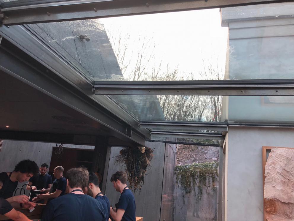 Photogallery






Noma 2.0 is in Christianshavn, the same neighbourhood as the first Noma. They’re 1.5 km apart, a 15 minutes’ walk. This picture shows the distance: to the right, there’s the warehouse of the old location (in Strandgade 93), to the left the smokestacks of Amager Bakke, the futuristic incinerator below which stands the new Noma (in Refshalevej 96)









Weather permitting, you can have a peaceful walk between the previous Noma to today’s Noma 









The new Noma is on an isthmus surrounded by canals. In the future they also want to reclaim some small parts for hydroponic farming









Bucolic scene with incinerator









Bikes left outside Noma. It’s the favourite means of transport among employees and interns









The long path taking you to the restaurant. The fence on the left shows how works are still in progress









On the two sides of the path there are the two new sections of the "Noma village", each with its specialty: grill, hot dishes, snacks, fermentations... In one month’s time, behind the fence we’ll have greenhouses, the test kitchen and the bread making area









To the left, before arriving at the restaurant, the future test kitchen. This will be run by Danish Mette Søberg with Riccardo Canella. "My first challenge?", reveals the latter, for a long time sous chef here, "is to work on the extraction of essential oils" 









The future Test Kitchen









The temporary gangway to the restaurant









Looking from the door to the restaurant, there’s a lake and the smokestacks puffing vapour from the Amager Bakke incinerator. It’s a futuristic project, both in terms of sustainability and architecture. It’s also known as Amager Slope or Copenhill, and its author is starchitect Bjarke Ingels, the same who designed the new Noma. Gradually opened in 2017, it transforms waste into electricity. The goal is to donate electricity to 62500 houses and hot water to 160000. It’s part of an ambitious project to transform Copenhagen into the first city in the world in terms of zero carbon dioxide emissions by 2025. By autumn this year, Amager Slope should open its ski slope, a climbing wall and a hiking track. You’ll be able to slalom on top of the incinerator









The windows from the dining room









Work is still in progress (photo taken on Thursday 22nd February 2018)









Traces of the old building, with barbwire. During WWII, they built bombs here









A view of the dining room at night (photo from Instagram/James Spreadbury)









The entrance to the restaurant









The usual ritual: a welcome from the entire staff, led by Rene Redzepi 









Behind the entrance, there are formaldehyde tanks with creatures from the abyss, shaped as in Damien Hirst’s works. The first image once you’re inside is to reproduce a Scandinavian village









The service kitchen is larger, more spacious and a completely open view from the dining room: "It’s the heart of our Scandinavian village", says Canella. There are 30 cooks working here now. 10 more, compared to the previous Noma






