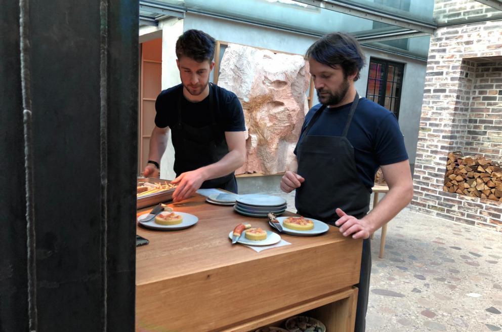 Photogallery






Noma 2.0 is in Christianshavn, the same neighbourhood as the first Noma. They’re 1.5 km apart, a 15 minutes’ walk. This picture shows the distance: to the right, there’s the warehouse of the old location (in Strandgade 93), to the left the smokestacks of Amager Bakke, the futuristic incinerator below which stands the new Noma (in Refshalevej 96)









Weather permitting, you can have a peaceful walk between the previous Noma to today’s Noma 









The new Noma is on an isthmus surrounded by canals. In the future they also want to reclaim some small parts for hydroponic farming









Bucolic scene with incinerator









Bikes left outside Noma. It’s the favourite means of transport among employees and interns









The long path taking you to the restaurant. The fence on the left shows how works are still in progress









On the two sides of the path there are the two new sections of the "Noma village", each with its specialty: grill, hot dishes, snacks, fermentations... In one month’s time, behind the fence we’ll have greenhouses, the test kitchen and the bread making area









To the left, before arriving at the restaurant, the future test kitchen. This will be run by Danish Mette Søberg with Riccardo Canella. "My first challenge?", reveals the latter, for a long time sous chef here, "is to work on the extraction of essential oils" 









The future Test Kitchen









The temporary gangway to the restaurant









Looking from the door to the restaurant, there’s a lake and the smokestacks puffing vapour from the Amager Bakke incinerator. It’s a futuristic project, both in terms of sustainability and architecture. It’s also known as Amager Slope or Copenhill, and its author is starchitect Bjarke Ingels, the same who designed the new Noma. Gradually opened in 2017, it transforms waste into electricity. The goal is to donate electricity to 62500 houses and hot water to 160000. It’s part of an ambitious project to transform Copenhagen into the first city in the world in terms of zero carbon dioxide emissions by 2025. By autumn this year, Amager Slope should open its ski slope, a climbing wall and a hiking track. You’ll be able to slalom on top of the incinerator









The windows from the dining room









Work is still in progress (photo taken on Thursday 22nd February 2018)









Traces of the old building, with barbwire. During WWII, they built bombs here









A view of the dining room at night (photo from Instagram/James Spreadbury)









The entrance to the restaurant









The usual ritual: a welcome from the entire staff, led by Rene Redzepi 









Behind the entrance, there are formaldehyde tanks with creatures from the abyss, shaped as in Damien Hirst’s works. The first image once you’re inside is to reproduce a Scandinavian village









The service kitchen is larger, more spacious and a completely open view from the dining room: "It’s the heart of our Scandinavian village", says Canella. There are 30 cooks working here now. 10 more, compared to the previous Noma









Large skylights above the cooks









There are currently more than 100 people working at Noma, of whom 63 are cooks - 26 employed, and 37 as interns









There’s fire in the kitchen, for the first time









On average, the dining room can host 40 people. "However", complains Redzepi, "there’s always someone who turns up with more people than the ones booked"









While the dining room is set, the outside space still need to be defined









The staff made the dining room decorations. There are no overly expensive designer objects









Dried fish









Seaweeds hanging from the ceiling









Dried octopus heads preserved in salt (with a balloon inside)














Bjarke Ingels and Redzepi’s plan included the wish to recreate a Danish farm









The luminous private dining room









The counter in the dining room. They drew the beams from the canals around the restaurant














The mise en place, bare and strictly without tablecloths









Water jug, candle, flower vase









A warm cloth, to begin with









Australian James Spreadbury, restaurant manager and partner at Noma









Welcome drink: Champagne extra brut Blanc d'Argile from Domaine Vouette et Sorbée









Sea Snail broth. The welcome dish at Noma is, as usual, a hot “soup”









Stefano Ferrano, from Torino, presents the following dish. There’s always a large Italian colony at Noma









Venus clams. Molluscs from Limfjord (Denmark) mixed with decorative clams, typical of Noma. Beside them, shells with blackcurrant oil and “Danish curry”, made with toasted coriander seeds, fennel and fennel seeds









The lid above the following dish. The mussels are not edible









Best of the mussel. Mussels open in a pan with water of fermented barley. «We recreate the mussel», says Canella, «using just the flaps, the best part». The paste is made with scraps from the mussel, cooked in smoked butter









The next dish is conceived and served by Riccardo Canella, the Paduan sous chef who conquered Redzepi, here with dining room intern Feline Hansen









Dried fruits and shrimps. In this case, the heads are not a decoration, but you must suck them –best not eat them because of the bones: they’re filled with a lovely prawn cream. The small crustaceans are still alive when they arrive on a ship straight from the Norwegian fjords









Inside, under the prawn broth skin, there’s fruits and vegetable preserved from the previous summer with raw prawns and gooseberry sauce with blackcurrant oil









How about beverages? There are three options, as usual: wine pairing (6 glasses plus a beer plus sake, 150 euros), juice pairing (juices and extracts, 110 euros) or a choice from the list. They recommend Champagne Chut... Libre from Val'Frison pour Dominique Derain, 50% Pinot Noir, 50% Chardonnay created by a couple who met at the old Noma. Well bodied, it will be a good match throughout the meal









As usual, the wine list starts with Champagne: the cheapest is 1400 crowns (190 euros)









White wines begin with labels from cold climates: first Austria, increasingly popular for its natural wines, then Germany, then all the others









How about Italy? Few names, among the white wines, from North and South









A dozen red/orange wines









Sea star, that is to say Cured trout roe and eggs, the emblem dish of this new era. They recommend moving the teaspoon from the heart to the edges of the tentacles. Aesthetics win over taste









Jellyfish. The jellyfish gel in the middle is in fact a clarified broth of calamari and recalls the texture of jellyfish. "We tried to cook jellyfish in 300 different ways but none was convincing so far". All around, pickled seaweed. The gel is almost tasteless, it serves to clean the palate after the pickles









Rene Redzepi himself presents the content of the first Seafood platter.









French style service with a small plate below for the empty shells









It’s made of two (per two) pieces: queen clam and mahogany clam









The Queen Clam is a very small variety of Norwegian scallop, seasoned with a vegetal reduction made with cucumber and peas miso. The red tip is the coral. "You should eat it using the top shell ", recommends Redzepi









The Mahogany clam is a centennial clam from the North Sea, very popular in Denmark and Iceland. «You can tell the age by the number of rings, like with trees», says Redzepi, «In 2007 they found one that was 450 years old. We’ve had it in the menu for a decade or so». The razor clam shell serves as teaspoon









Inside, there’s obviously not just a bare Mahogany. «We open it when the client arrives», says Canella, «remove the entrails and then slice it so as to preserve its firm texture». It’s seasoned with stir-fried gooseberry, capers of blackcurrants and blackcurrant sprouts preserved in vinegar. The sauce is made with mussel water









A note on the chairs: they’re more minimalistic. They’re no longer covered in sheepskin or leather from other Danish animals, in the style of Noma 1.0. The most significant element is the napkin: if you go to the toilet, they no longer replace it with a new one. There’s the old one, tied to the chair. "This is sustainability", they explain









The second seafood platter. It’s made of Sea cucumber and sour cream in various textures, including «chicharrones» (at 9 o’clock), sea urchins (at 12 and 3) and gigas oyster (at 6)









Sea urchins pressed in fresh cream and pumpkin seeds









Giga Oyster, a huge oyster from the Pacific, quickly steamed and garnished with pickles. Noma only reserved one thousand of these. In the menu until available









The following dish, off the menu, is again from Canella: horse mussel ragout, rare specimen of which 30 arrive at 'Noma each week









They cook the mussel as if it were kidney, in a sort of Bolognese sauce but with ginger. Ginger? "Yes, we’ve decided to include it, as with other spices, after our Mexican experience"









Another Italian presents a dish, Edoardo Fiaschi from Prato, at Noma for 3 years now









Squid in seaweed butter. An almost neglected Danish squid lightly seared in fermented koji oil, rolled and seasoned with seaweed butter and served on sticks of blackcurrant that widen its aromas. Formidable and beautiful









The following dish is inside a nice bee wax container. It’s made with balloons covered multiple times in bee wax. «We spent weeks making them. We’ve made thousands». They’re disposable...









Sea snail and roses. They recommend to: "Eat it keeping the bee wax on your hands "









Sea snail. Another small nibble from the top part of the sea snail, lightly warmed up in water and served on a reduction of lemon thyme









A sea snail toothpick, initially carved by Redzepi himself









Head of the cod, (right), the real main course at Noma









Another rather laborious recipe. «It takes half an hour just to separate the head. We remove the skin, the collagen, we cut mandibles, tongue, cheek and the part behind. We rinse it in water, spices, koji and cook it in the yakitori with a glaze of mushrooms and spiced fennel broth»









You can garnish the cod as you choose, with a paste of ants (top right corner), a slightly spicy emulsion of koji oil, water and horseradish sauce (left) and Danish curry (bottom)









On the side of the cod, there’s also wild garlic seasoned with smoked butter and roasted yeast. Intense flavour









Cod bones after the tasting









An interlocutory snack made of cod cheek









Pickled vegetables and arctic herbs. The only vegetable dish in the menu, marks the passage from savoury to sweet dishes. Between June and August 2018 the menu at Noma will be 100% vegetarian









Preparation time: half an hour! A challenge for the person making it









Mussels appear once again, a classic emblem









This time it’s a dessert in the shape of a small sandwich. Pear and roasted kelp ice cream 









Cloudberries and pinecones. A dessert that continues Redzepi’s saga of unsweet sweets: cloudberries, pinecones preserved in sugar, yogurt snow (by Italian Jessica Natali) and a sea snail made with cloudberry sorbet









Filtered coffee made with stolen kenyoti seeds farmed in Honduras by a Norwegian guy. Italian sommelier Francesca Niro tells us this story. «In Denmark», she says, «coffee is not a final act»









Sugar kelp tart. Tartelletta di alga kelp con pralinato di pino (sul modello di quello di mandorle, autore Canella), panna e crisp di ostrica









Sugar kelp tart. Jessica Natali, 23, from the March, has been at Noma for 4 years now









Natali introduces the last dish, Plankton cake







