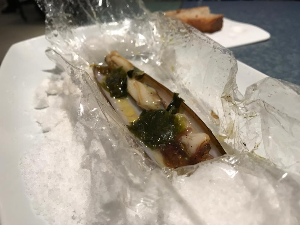 Galleria fotografica






L'inizio di un percorso meraviglioso: Lengua helada de pasión con ron, ossia una lingua di gatto gelata al rum, frutto della passione e menta piperita. Inizia il gioco di temperature









Rosa & lichis: poesia pura. Sferificazioni di acqua di rose (sui petali laterali) e finta mora ghiacciata di lichi









La remolacha que sale de tierra: insieme sorbetto e meringa di barbabietola









Panchino relleno de caviar beluga: uno dei piatti signature del Disfrutar. Si prepara una pasta per brioche con molta acqua e lievito. Viene collocata in un sifone e si ottiene una schiuma. Quindi si riempie il fondo di uno stampo circolare con questa schiuma, si aggiunge il caviale e una crema doppia panna, quindi ancora schiuma per coprire il tutto. Si immerge in una padella con olio a 180 gradi per 20 secondi. Ovviamente il caviale può essere sostituito da formaggi, tonno, sorbetti...









La preparazione al tavolo del Sidra casera ahumada al momento, un sidro di mele istantaneo: si versa sul ghiaccio secco una mistura di liquore e succo di mela e si lascia agire









Inizia il tributo alle noci. Qui il gheriglio, ricostruito, custodisce un quarto di noce, affumicata. E deliziosa. In pratica il guscio è stato aperto, senza romperlo; la noce è stata affumicata, poi rimessa al suo posto, il tutto richiuso









Ancora Cáscara de nuez: qui è un tripudio. Una noce tenera, senza pelle, l'altra verde col gheriglio e resa commestibile, infine l'ultima cotta e macerata nel ratafià, come abbiamo già spiegato nel pezzo. Il tutto con un filo di latte di noce e di olio di frutta secca. L'idea è: con un prodotto possiamo costruire all'infinito









Candy salado de nueces con mango, haba tonka y whisky: la bustina commestibile contiene caramello salato e noci, quindi il mango crudo e il profumo del whisky affumicato









Milhojas de idiazábal, millefoglie di idiazábal, un formaggio basco. Sterzata salata dopo una prima parte di degustazione in cui prevalevano le note dolci (a esaltare anche il caviale del Panchino). In generale, sono tutti piatti che superano la tradizionale distinzione dolce/salato









"Hostia" de flor del mandarino: la finta ostia è di ovulato, racchiude essenza di fiore di mandarino. Un piatto che colpisce il cuore









La Gilda del Disfrutar. La gilda è il classico pincho che si serve nei Paesi Baschi, a base di olive e acciughe. Qui abbiamo le celebri false olive di Adrià, croccanti fuori (burro di cacao) e liquide all'interno. Poi sgombro marinato, semi di pepe basco e la loro crema









Sandwich de gazpacho con guarnición olorosa de vinagre de Jerez: qui il falso pane ghiacciato (sono meringhe di pomodoro secco) racchiude una farcitura in cui emergono le note acide e aromatiche dell'aceto di Jerez a esaltare il classico aroma del gazpacho andaluso









Almendras "supertiernas" en vinagreta: al Disfrutar giocano molto con la frutta secca, qui mandorle ammorbidite o croccanti e accompagnate da aromi di vaniglia, aglio, olio, vinaigrette... Altro capolavoro









Yema de huevo crujiente con gelatina caliente de setas: una crema d'uovo in tempura, croccante fuori e liquida dentro, sopra un gel di funghi racchiuso nel guscio dell'uovo stesso. «Per noi è un classico - ci dicono - Ma sempre molto difficile da gestire»









Piatto spettacolare e gentile, Tatin de foie-gras y maíz multiesférico: tutto giocato su un equilibrio in cui le note dolci sono spinte al limite. La tecnica è quella della multisferificazione, con gel di glutammato a chiudere la partita









Ceviche en deconstrucción: leche de tigre, emulsione di pesce, olio di coriandolo e sorbetto di zucca e ajì. Un classico del Disfrutar

 









Questa è la cartilagine del muso del salmone...









...protagonista di quest'altro piatto, nuovissimo: il collagene del muso del salmone con le sue uova e salsa di acetosella. Wow!









Altra novità, presentata a Gastronomika, è la Costilla de salmón con mojo di estragón. Le costolette di salmone, ottenute una a una sfilettando con attenzione le lische con la polpa attorno, sono accompagnate da mojo di dragoncello e uova di salmone






