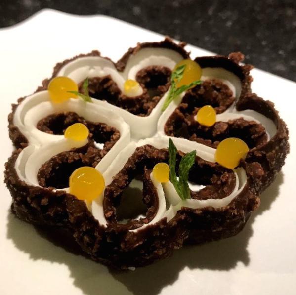 Galleria fotografica






Consommè de garbanzos. Prima che cominci il menu degustazione, viene portata al tavolo una bottiglia di vetro contenente del brodo freddo di ceci (in alto a destra). Ventitrè piatti dopo, alla fine del percorso "salato", verrà versato, in un bicchierino da grappa, del brodo caldo di jamon iberico da una teiera. Sopra ancora, la schiuma del brodo di ceci. Un caldo-freddo speciale (foto @ticketsbar instagram)









Tosta de pollo y anchoa. Primo piatto: toast di pelle di pollo con lisca di acciuga. A lato, una crema di acciughe composta da burro e pasta di acciughe









Olive Gordal. Uno dei simboli della saga Adrià: le olive sono immerse in un liquido d'olio extravergine d'oliva, cannella, buccia di limone e anice stellato. Si tirano su con un cucchiaino forato, si poggiano su una conchiglia di legno a lato e da qui in bocca. Gordal è una varietà dall'Andalusia









Prima preparazione rifinita al tavolo: Polo de almendras









Polo de almendras è uno stecco di gelato al latte di mandorle, spennellato sul posto con olio d'oliva e cosparso con granelle di mandorle, fiori di sambuco e sale. E' servito su un piatto con cubetti di ghiaccio. Dolce(salato) e gelato all'inizio del pasto e non alla fine, uno schema molto Adrià









Coliflor y caviar. Ganache di cavolfiore e caviale russo Schrenkii









Gamba a la sal fría. Gamberi marinati nel tè Lapsang Souchong con zest di bergamotto. Sono serviti su un vassoio con "neve di sale" per ricordare il ghiaccio tipico di un mercato del pesce









Atún con cerezas. Tonno e ciliegia: ventresca di tonno confit in grasso di prosciutto, accompagnata da una ciliegia affumicata (senza nocciolo)









Ceviche de melón cantaloup. Ceviche di melone cantalupo con succo di lime, coriandolo e leche de tigre di kumquat. Servito con kumquat, olio di coriandolo e neve di kumquat. Citrico alla terza









Pizza crujiente. La "pizza" di Tickets: millefoglie di regañà (torta di pane croccante di origini andaluse), stracciatella, bottarga e fichi









Porex de Calix. Marshmallow di dashi ripieno di crema acida e sormontato da caviale di Kalix, uova rosse svedesi di coregone, dalle note dolci ed eleganti









Nigiri de berenjena. Nigiri di melanzana









Cubo de wagyu. Cubo di chips di patata croccante con sopra una tartare di wagyu trattata con olio, sale, senape di Digione, uova e pepe. Una magnifica tapa da circa 2 cm per lato, che ricorda le battute al coltello della tradizione piemontese









Milhojas de atún. Millefoglie di tonno: millefoglie di patata e alga nori. In cima, tartare di tonno leggermente piccante con crema di avocado









Miniairbag de queso. Miniairbag di spuma di formaggio manchego, caviale di nocciola e polvere di buccia di nocciole









Airbaguette de rubia gallega: grissino-baguette vuoto avvolto da fettine di "prosciutto" marinato di rubia gallega, pregiata razza bovina galiziana









Encerradito de buey: involtino di ravioli di avocado con dentro granciporro con maionese di peperoncino chipotle e gelatina di coriandolo. Sotto c'è del pane sardo guttiau, sopra dei semi di chia. Un assaggio cremoso, grasso e vegetale in due bocconi magnifici









Foie y anguila. Foie gras d'anatra di Mitteault ripieno di anguilla avvolta in alga nori









Espardeña con panceta. Cetriolo di mare con la sua pelle fritta e wasabi, sopra una striscia di pancetta di prosciutto Joselito. Forse l'unico punto di domanda









Pulpo crujiente. Octopus tenero in panko (pangrattato giapponese piccante) croccante, accompagnato da cetrioli baby pickled









Cogollo con sorbete. Seconda preparazione rifnita al tavolo: cuore di lattuga accompagnato dal suo sorbetto ghiacciato con zest di rafano









Bogavante. Astice. L'unica non-tapa di tutto il percorso









Arriva il calice col Consommé freddo di ceci che rimane spumoso in cima e, sotto, il brodo caldo di jamon iberico (vedi prima slide)









Ci si alza dal tavolo e si va alla Dolça di Tickets, l'ambiente in cui si chiude il percorso coi dessert (foto elequipocreativo)









L'accoglienza nella Dolça? Una rosa che regge la sfera rosa: lychees e fragola









Coco. Gelatina di cocco, sorbetto al lime e cocco e acqua di curry









La celebre Cheesecake di Tickets. La buccia della "toma" a sinistra è composta da cioccolato bianco e crema di nocciole. Nel ripieno, una favolosa crema di brie. Accanto, biscotti di nocciole. Un carrello di formaggi trasformato in dessert









Mini pancake. Terza preparazione al tavolo: pancake croccante alla fragola e spuma di panna montata congelata






