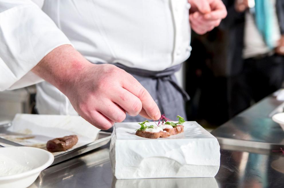 Galleria fotografica






ALFIO GHEZZI – Microclima: la distanza che accomuna - Fedele a se stesso e al titolo della sua lezione Alfio Ghezzi ha presentato la Tartiflette alla mia maniera, «una rivisitazione del frico, del rosti e della tartiflette; ma ho trovuto preparazioni simili anche in Norvegia», spiega. Per la sua tartiflette utilizza crema di patate, mortandela e un formaggio di pasta ottenuto dalla fermentazione di polvere di pasta precedentemente cotta in acqua per 50’ a 96° e poi essiccata in forno per un’intera notte









L’ingrediente principale del secondo piatto è lo yak della Val d’Ambiez, discendente dai buoi tibetani portati in Italia da Reinhold Messner, di cui Ghezzi ha impiattato la carne affiancandola a un crostino di pane di segale con lardo dello stesso yak, polvere di trombette nere, paprika affumicata, e - servito in tazza - a un brodo di carne di yak caramellata con miele e erbe









RICCARDO GASPARI con OLIVER PIRAS e ALESSANDRA DEL FAVERO Il “trip” del latte -Nell’agriturismo El Brite de Larieto l’alta cucina di Gaspari si sposa con le materie prime dell’allevamento di famiglia









Il salame di piedino di maiale con la sorpresa di un cubetto di lingua al suo interno cui fanno da cornice una gustosa di crema di siero di latte e nocciole tostate, sovrastato da una granita di mela (che dà una nota unica al piatto) e fiori di rosmarino è la summa dell’enunciato che nessuna materia è povera quando la si lavora a dovere. Il piedino di maiale è cotto nel latte, disossato e lavorato come un salame, da conservare al freddo «perché tende a spezzarsi». Il tocco finale è dato dal crumble di porcini e dalla rapa marinata









Bastano venti minuti per spostarsi da El Brite all’Aga di Oliver Piras e Alessandra Del Favero, ma l’ispirazione della cucina di Piras (sardo adottato dal Cadore in cui è stato spinto dall’amore) e Del Favero, coppia in cucina e nella vita, è diversa. Si capisce subito dal tiramisù, che di fatto non lo è pur ricordandone i sapori, ispirato da un loro viaggio in Giappone e dalla scoperta del koji, fungo utilizzato per la fermentazione della soja e del riso per fare miso e sake. Il dolce di Oliver e Alessandra ha una base di polenta di orzo di Belluno (presìdio Slow Food) fermentato e bruciato, è aromatizzato con infusione di radici di cicoria e completato da gelato di koji fatto con latte di El Brite









MAURIZIO GRANGE E PIERGIORGIO PELLEREI - I piatti della nostra tradizione visti con gli occhi della contemporaneità - Si può viaggiare anche rivisitando la tradizione. È un viaggio nel tempo quello di Maurizio Grange e Piergiorgio Pellerei fanno fare al piedino di maiale









Rosolato intero con sedano, carote e cipolle e poi cotto in un fondo di vitello per 2/3 ore prima di venire disossato, il piedino diventa con i carciofi il ripieno per il raviolone saltato al burro alle erbe. La presentazione è su una salsa di cavolfiori e zenzero deliziosamente piccante









ANTONIO BIAFORA E NINO ROSSI - Transumanza: istinto ancestrale di sopravvivenza - Biafora e Rossi hanno dato al tema del viaggio un significato diverso: per i due calabresi è un percorso per la sopravvivenza. Quello degli uomini che in Calabria si spostavano con le loro bestie dalla montagna al mare e viceversa in quella transumanza corta che ha contaminato i sapori









I piatti di Biafora e Rossi sviluppano il concetto di altura con elementi di mare, collina e montagna. Il primo impatta la “riunella” (una trippa di vitello arrotolata in budello di capra glassata in un fondo di vitello, capra e rosolato col burro) con sarda dissalata, una salsa di cavolo in salamoia, aghi di pino e pistacchio e completato con polvere di buccia di limone






