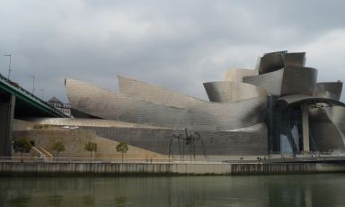 Il museo Guggenheim di Bilbao visto dall’altra sponda del fiume Nervión. Davanti, al centro, il grande ragno di Louise Bourgeois, mentre all’estrema sinistra si nota la piccola scalinata che porta al ristorante Nerua, appena sopra c’è la terrazza dove poter trascorrere qualche tempo per l’aperitivo.