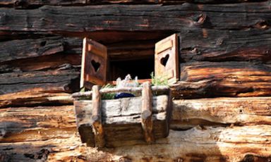La romantica finestra di una tipica, antica casa di montagna tutta in legno, con le ante forate al centro, fori a forma di cuore. Lo scatto è di Stefania Sainaghi che per il libro Cucina di Montagna - Le Alpi Centrali edito da Bibliotheca Culinaria ha lavorato sempre alla luce naturale, con risultati ottimi