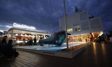 A night view of the entrance to the pavilion of the Czech Republic, with the swimming pool, the bar and the large sculpture purifying the water in the fountain 