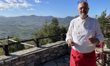 Michele Milani in veste di cuoco, con alle spalle il paesaggio della Val Luretta
