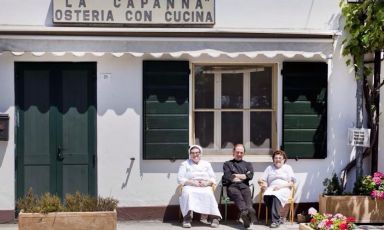 Maria Grazia e Pierluigi Soncini insieme alla madre Vanda, seduti davanti alla porta de La Capanna di Eraclio di Codigoro (Ferrara), insegna che rappresenta la storia della loro famiglia e che si tramanda di generazione in generazione
