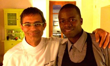 Roberto Petza, chef del ristorante sardo S'Apposentu, con Djime Sidibe. Il ragazzo maliano, in fuga dalla guerra civile del suo paese, dopo esser sbarcato in Italia come richiedente asilo, è stato preso in consegna dalla Ong Gus. Ha appena firmato un contratto part-time per lavorare in sala nell'insegna di Siddi, una stella Michelin (foto www.port-culinaire.de)