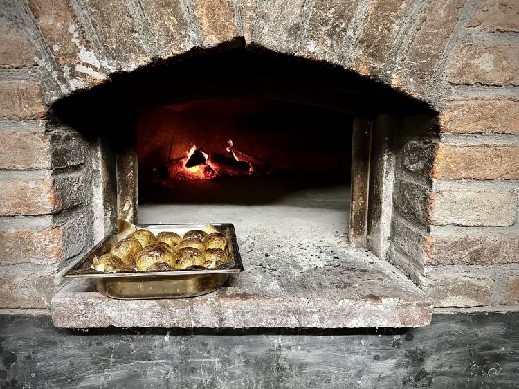Il forno a legna e una teglia di patate pronte per essere condite e portate in tavola