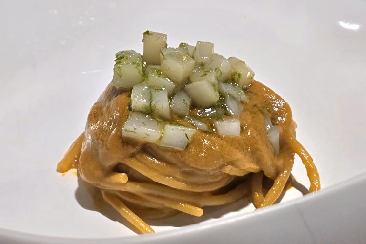 Spaghetto con ristretto di zuppa di pesce e seppia cruda. La zuppa nasce dal fondo ottenuto dagli scarti del pescato, in un raffinato lavoro di recupero che trasforma l’essenziale in gusto puro. Un piatto goloso e immediato, dal carattere schietto e marino
