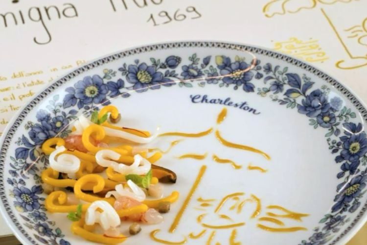 Omaggio alle stagioni del Charleston al mare nella struttura liberty di Mondello, Gramigna Lido: gramigna cotta in una concentrazione di pesci da zuppa, servita in tavola direttamente dalla pentola su una composizione di pesci marinati e una salsa concentrata di pomodori gialli e menta. La grafica è ispirata alla spiaggia di Mondello