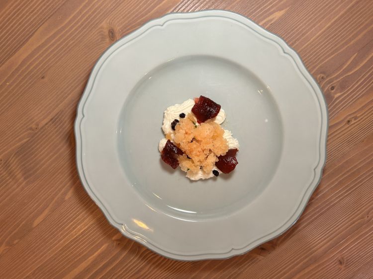 Ricotta montata, peperone candito, menta, pompelmo e olive. La ricotta viene montata con burro, zucchero e vaniglia. Alla base del piatto, falde di pepe rosa disidratato; poi peperone e oliva disidratati e glassati con sciroppo di zucchero. Al centro, olio extravergine d’oliva; a completare, mentuccia selvatica e una granita di pomodoro. Dessert fresco tra note lattiche e amaro/agrumate