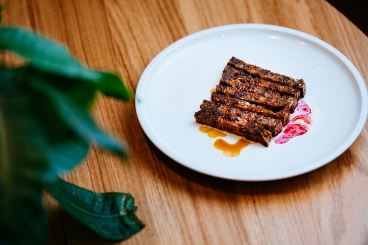 Tagliata di pane, un gioco sulla tagliata di carne, con fette di pane di segale tostato sui 4 lati, servito con un estratto di verdure, condito con olio all'aglio, ginepro e rosmarino fresco, estratto di barbabietola cruda infusa a freddo con anice e caffè

