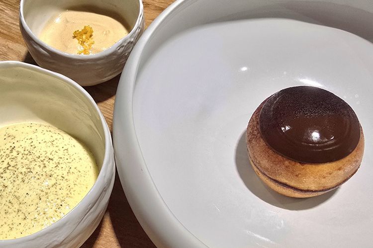 Brioche con cioccolato fondente ripiena di cioccolato al caramello servita con mousse di mascarpone e cardamomo verde e gelato al cioccolato al latte, caramello e arancia. In questo dessert goloso ma elegante, sontuosa chiusura della cena ideata dal pastry chef Alessandro Montanaro, la calda morbidezza della brioche incontra la cremosità speziata; equilibrio perfetto tra dolcezza, freschezza e note amare
