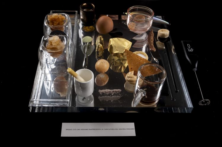 2019 - Illusione
«Un percorso con una serie di elementi che non corrispondevano esattamente a ciò che rappresentavano. Per esempio un coltello da passare sulla lingua con una finta lama stondata e nascosta da una crema spalmabili alla nocciola, un finto krapfen che nascondeva una nuvola di crema su una cialda croccante e molto sottile, un gianduiotto liquido, una finta mandorla liquida, un filo interdentale mentolato avvolto da cioccolato fondente che tratteneva alla sua estremità un cuscinetto croccante, due bicchieri di vetro con calamita nascosta che avvicinandosi si respingevano...»