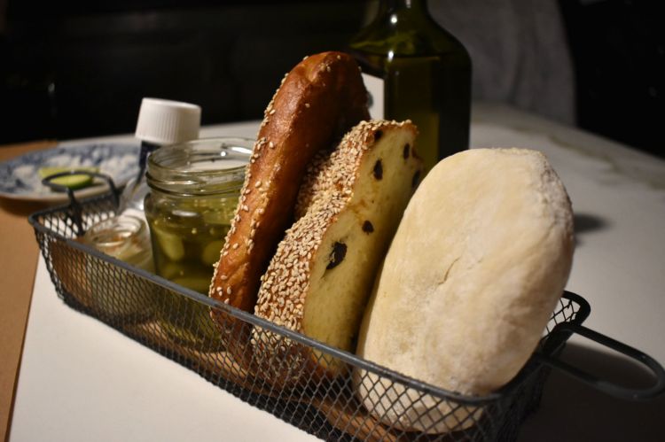 Il cestino del pane, a Mishiguene, è una sintesi molto efficace di quello che è la cucina judía.
Jerusalem bagel: tipico prodotto dei panifici arabi di Gerusalemme.
Jalá: è uno dei pani più importanti della tradizione ebrea, simbolo del giudaismo. È il pane tipico della tavola dello Shabbat (il sabato ebreo) e le sue origini risalgono ai tempi biblici. In Israele il pane Jalá intrecciato si vende in tutti i panifici ed esiste una panetteria nel quartiere di Mea Shearim, a Gerualemme, che dalla fine del XIX secolo produce esclusivamente pane jalá.
Pan Pita, conosciuto in Italia come “pane arabo”: una delle forme di pane più antiche della storia, utilizzato in Medio Orente, Turchia, India, Africa come posata per mangiare il cibo con le mani: essendo vuoto al suo interno è perfetto per raccogliere il cibo da portare alla bocca.
Cetriolini sotto aceto: tipici della cucina del Medio Oriente e Askenazi (nome dato alla popolazione judìa che si è stabilita nell’Europa Centrale e Orientale).
Patè di cipolla: tipico della cucina ebraica ashkenazita, con schmaltz (si tratta di grasso fuso, di pollo o di oca, viene utilizzato per cucinare e friggere) e gribenes (pelle del pollo cotto prima a bassa temperatura e poi fritta nel suo schmaltz).
