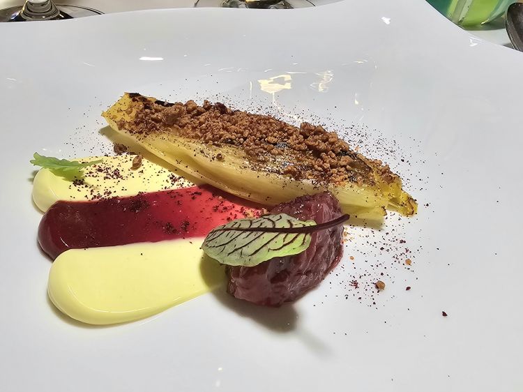 Indivia con lamponi, emulsione di zafferano e cioccolato. Profondo e intenso: indivia belga marinata e grigliata servita con un crumble al cioccolato, crema ai lamponi e un’emulsione di soia e zafferano