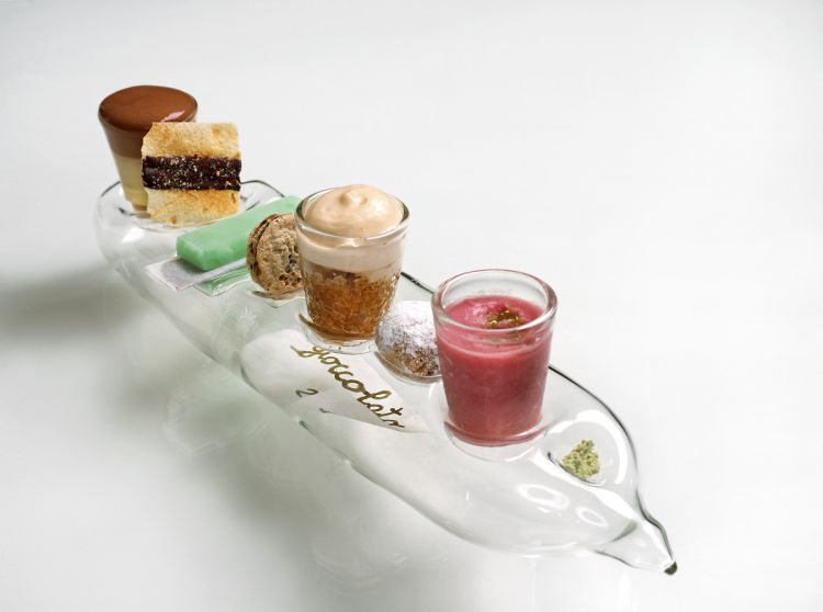 2004 - Gioccolato
«Scomodo e ideologico, proiettava attraverso la diluizione il potenziamento del cioccolato. Gli elementi di cioccolato erano pochi, uno solo esplosivo, gli altri non così ingombranti. La delicatezza sposava la raffinatezza, il vetro stesso ne caratterizzò la stoviglia, non a caso. La sospensione leggera del cibo e la bottiglia con il biglietto arrotolato portavano il messaggio di un cioccolato insolito, disatteso, quasi etereo»