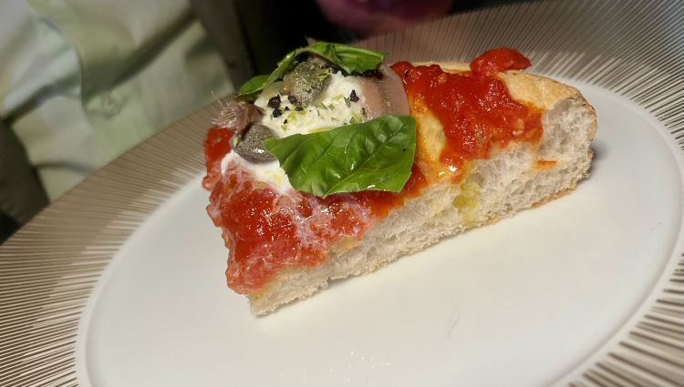 Contemporanea evolutiva alta (Marasco)
Pomodoro 100% italiano spadellato, stracciatella di vaccino pugliese, cappero di Salina sott’olio, filetto di acciuga sotto sale, polvere di olive di Gaeta, basilico fresco
L'impasto è figlio di un progetto di filiera che coinvolge grani siciliani. Il topping è pomodoro San Marzano ridotto, c'è aglio, basilico e olio extravergine d'oliva, stracciatella prodotta in Brianza (da Ghezzi), alice di Cetara e capperi di Salina dissalati, polvere di olive di Gaeta e basilico fresco. Prima della bontà ortodossa del condimento, colpiva il rapporto felice tra la croccantezza dell'esterno e la sofficità dell'interno dell'impasto
