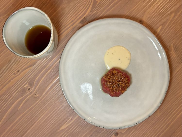 Pecora al pecorino, consommé di pecora. Per il battuto di pecora vengono utilizzate coscia e pancia, condite con strutto ottenuto dal grasso dello stesso animale. Sopra, ciccioli di pecora; accanto, una salsa di pecorino di fossa e un consommé di pecora, preparato con le ossa, chiarificato il giorno successivo con le parti meno nobili dell’animale, filtrato e aromatizzato al cardamomo verde. Il morso è quasi tiepido (plus) e fin troppo tritato (minus, per noi: manca un po' di masticazione), l'eleganza gustativa della pecora basterebbe quasi a sé stessa, col perfetto cardamomo, mentre la salsa è una scorciatoia golosa. Il brodo è sferzata sapida stemperata proprio dal cardamomo