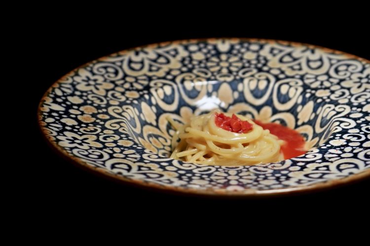 Spaghetto, burro affumicato, acciughe di Savona e fragole fermentate: uno spaghetto condito con burro locale leggermente affumicato e colatura ottenuta da acciughe di Savona (realizzata maison). A completare, fragole di bosco leggermente fermentate, capaci di sviluppare un’acidità quasi citrica. Un accostamento volutamente spiazzante tra grassezza, sapidità marina, fumo e componente fruttata-acida