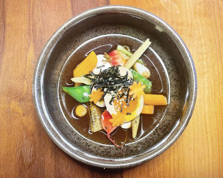 Uovo marinato in stile orientale con soia, cipollotto, miso, baby pannocchia, taccole, carote, tofu e cipollotto. Brodo: alga kombu, funghi shiitake, zenzero, cipollotto, sakè, mirin e soia