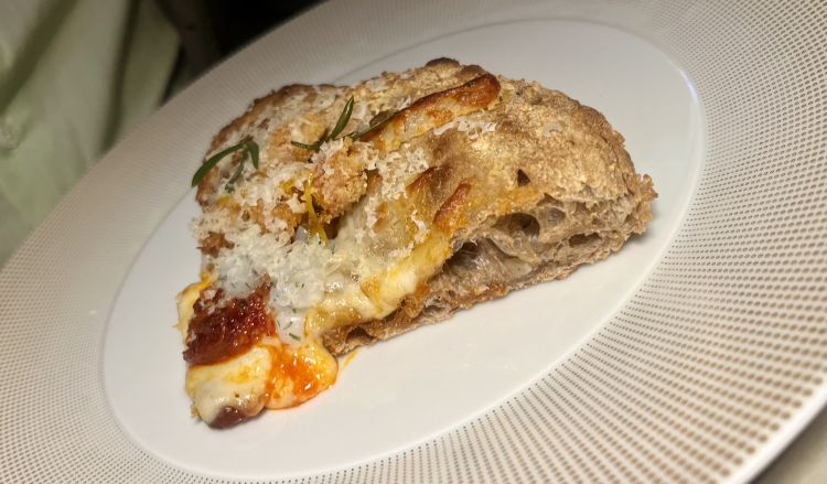 Contemporanea bassa agricola (Marasco/Sacchi)
Fior di latte d’Agerola, Sobrasada de Mallorca, formaggio Mahon, calamaro e limone
Il secondo spicchio, fantastico nella sua croccantezza e voluttuosità, è il frutto di una collaborazione tra i nostri due cuochi: l'impasto è di Marasco, il condimento di Sacchi. Il primo è ispirato al pane del Nord Europa: crosta scura e croccante, farina di segale, avena e farro, semenze (sesamo, girasole e mais), lievito madre ma non acido. Il topping, oltre al fiordilatte popolare di Agerola, girava attorno a ingredienti delle Baleari, cari al Sacchi. Formaggio vaccino semi-stagionato e sobrasada (insaccato tipo 'nduja ma dolce, non piccante) sovrastavano piacevolmente calamari, tagliati a dadini a marinati nel keffir lime e in forma di chipirones fritti. Abbiamo chiesto il bis (e avremmo chiesto pure il tris)
